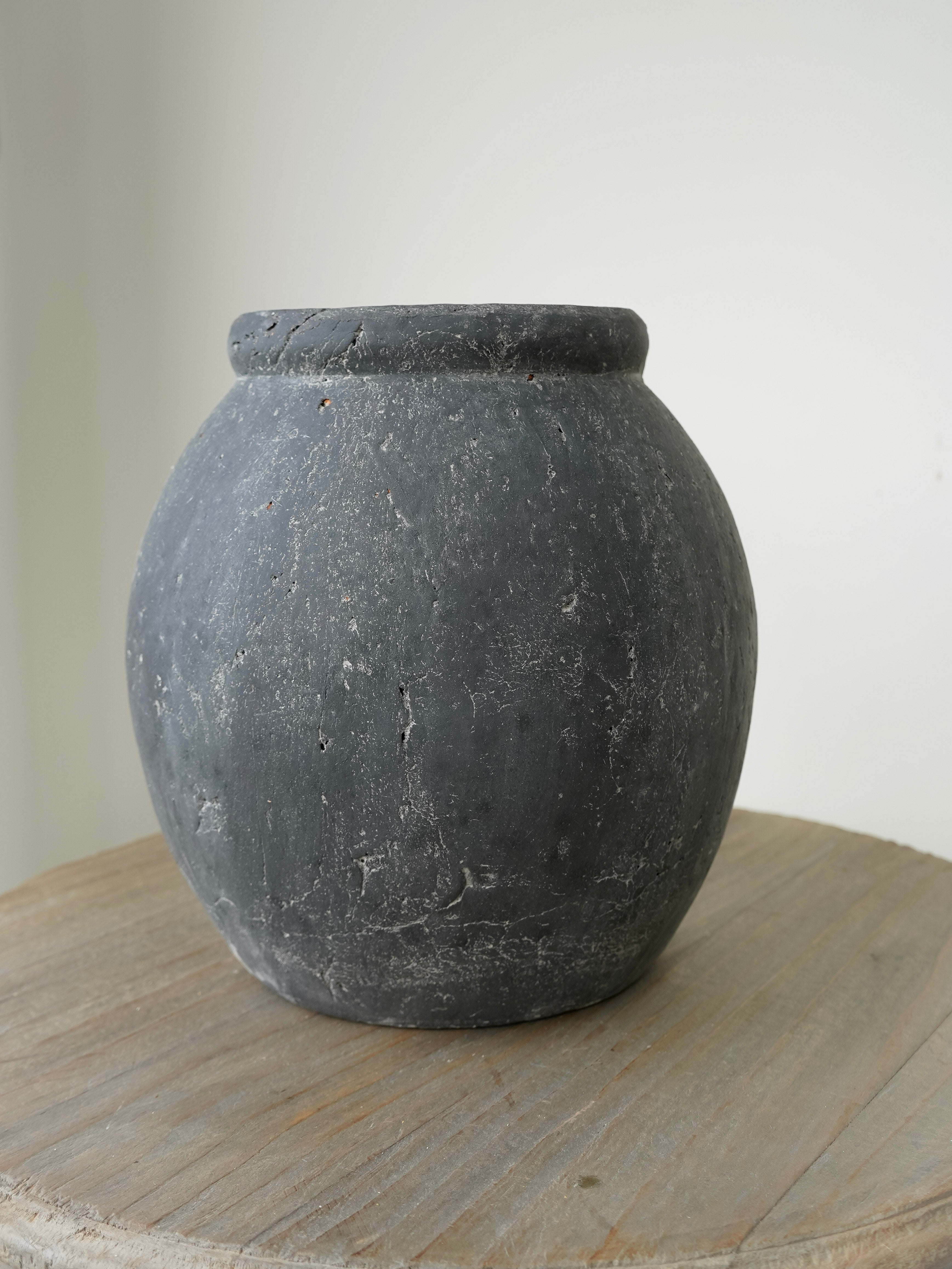Dark gray ceramic jar on a wooden surface with a plain background