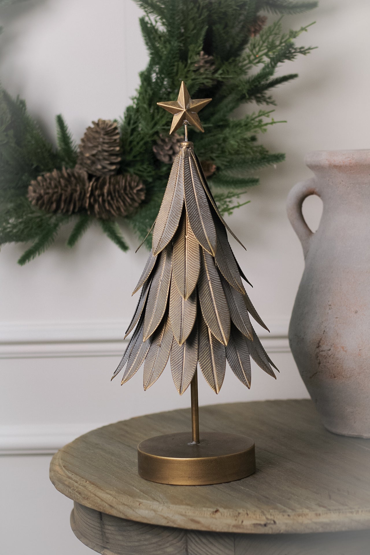 A decorative metal Christmas tree with a golden finish and leaf accents displayed on a wooden surface.