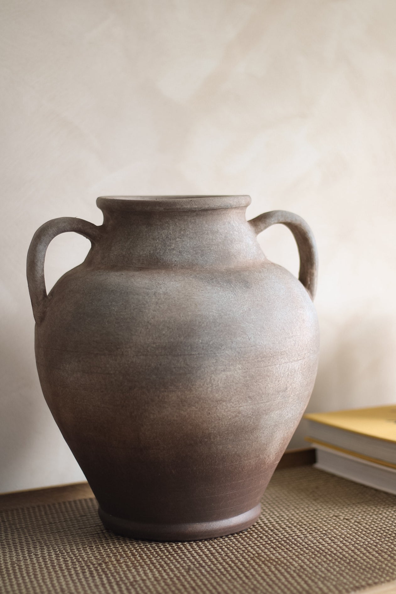Large brown ceramic vase with handles on a textured surface.