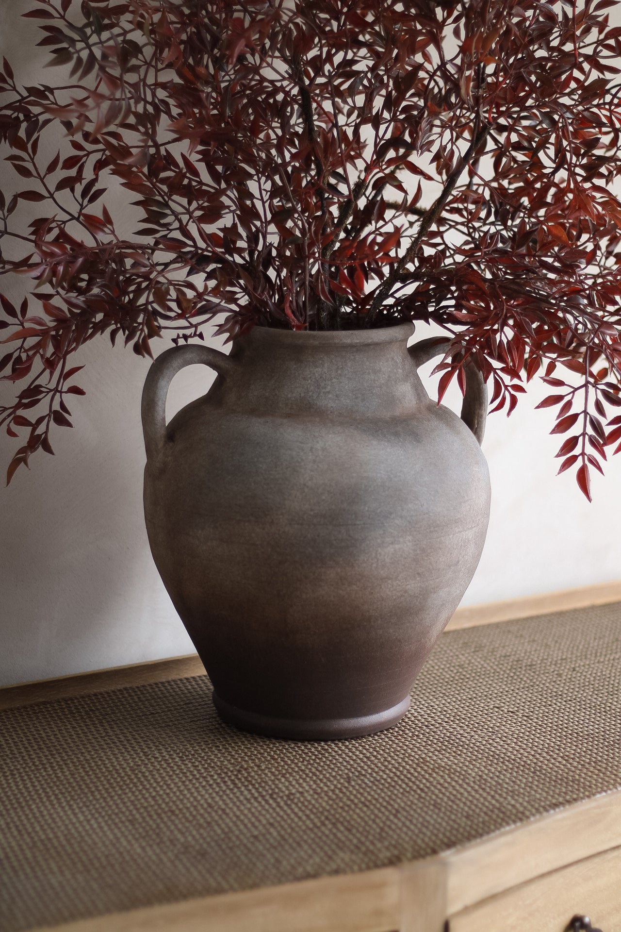 Decorative vase with red leaves on a textured surface