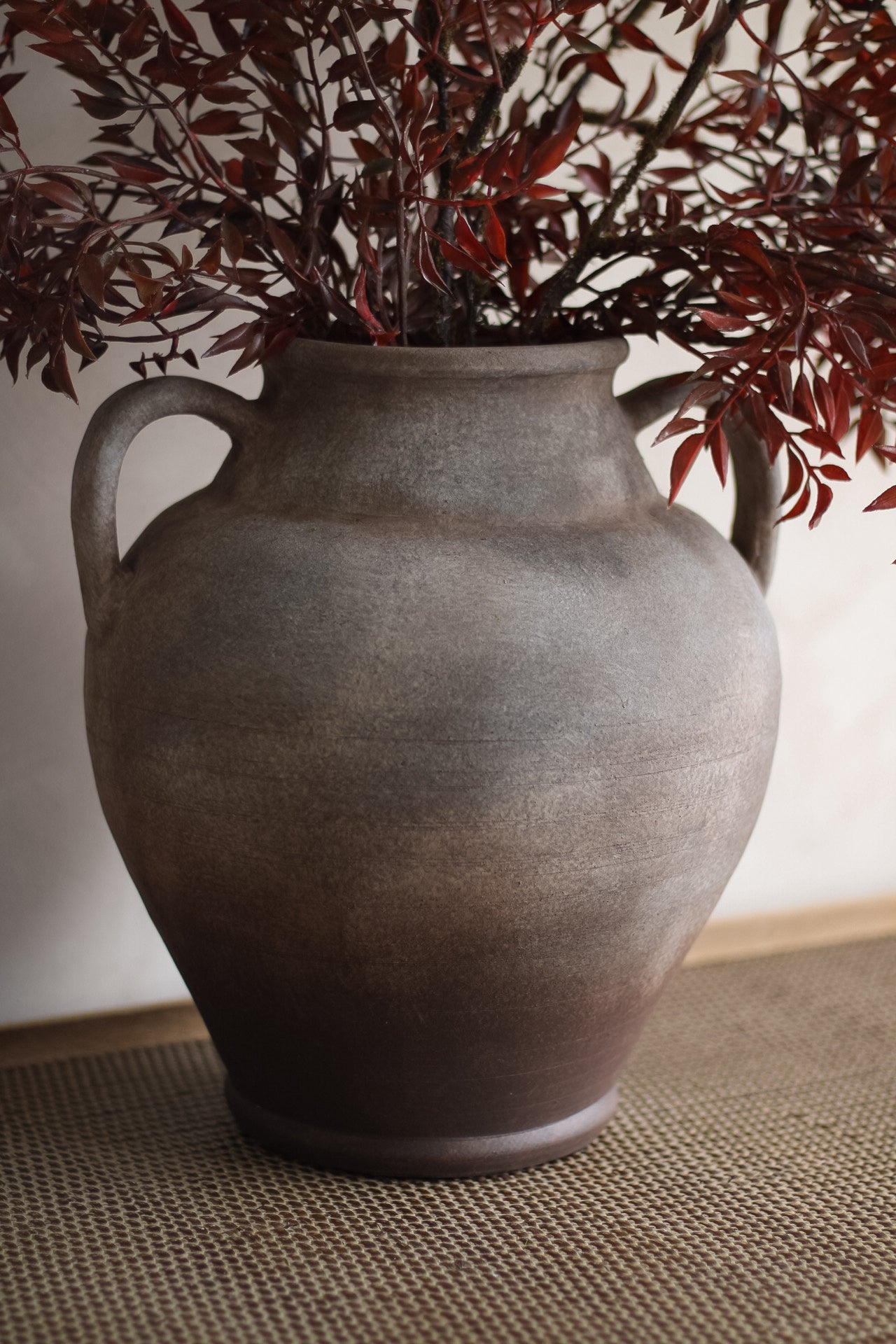 Mottled ceramic vase with red leaves on a textured surface