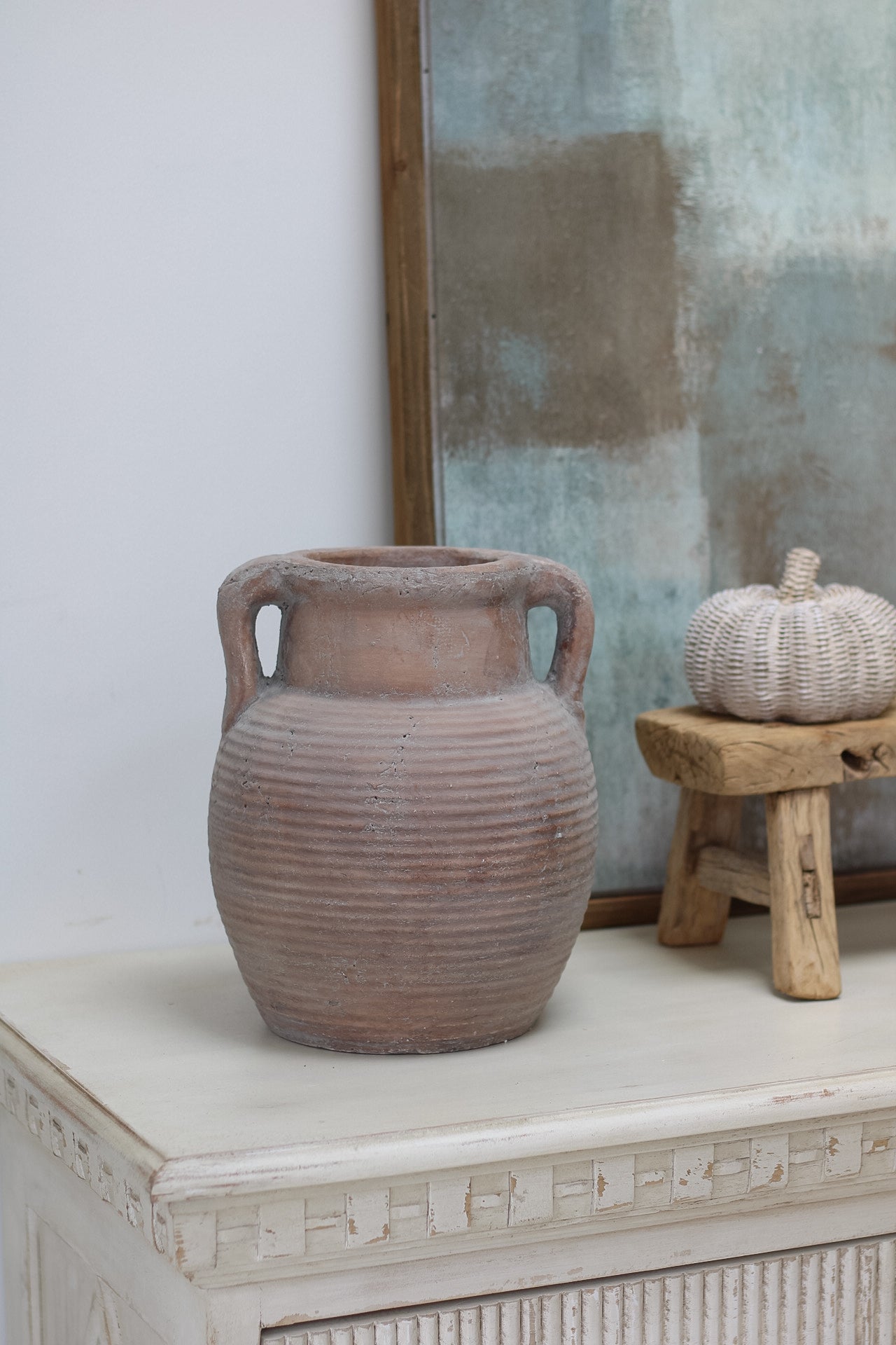 Terracotta vase on a white surface with a textured wall in the background