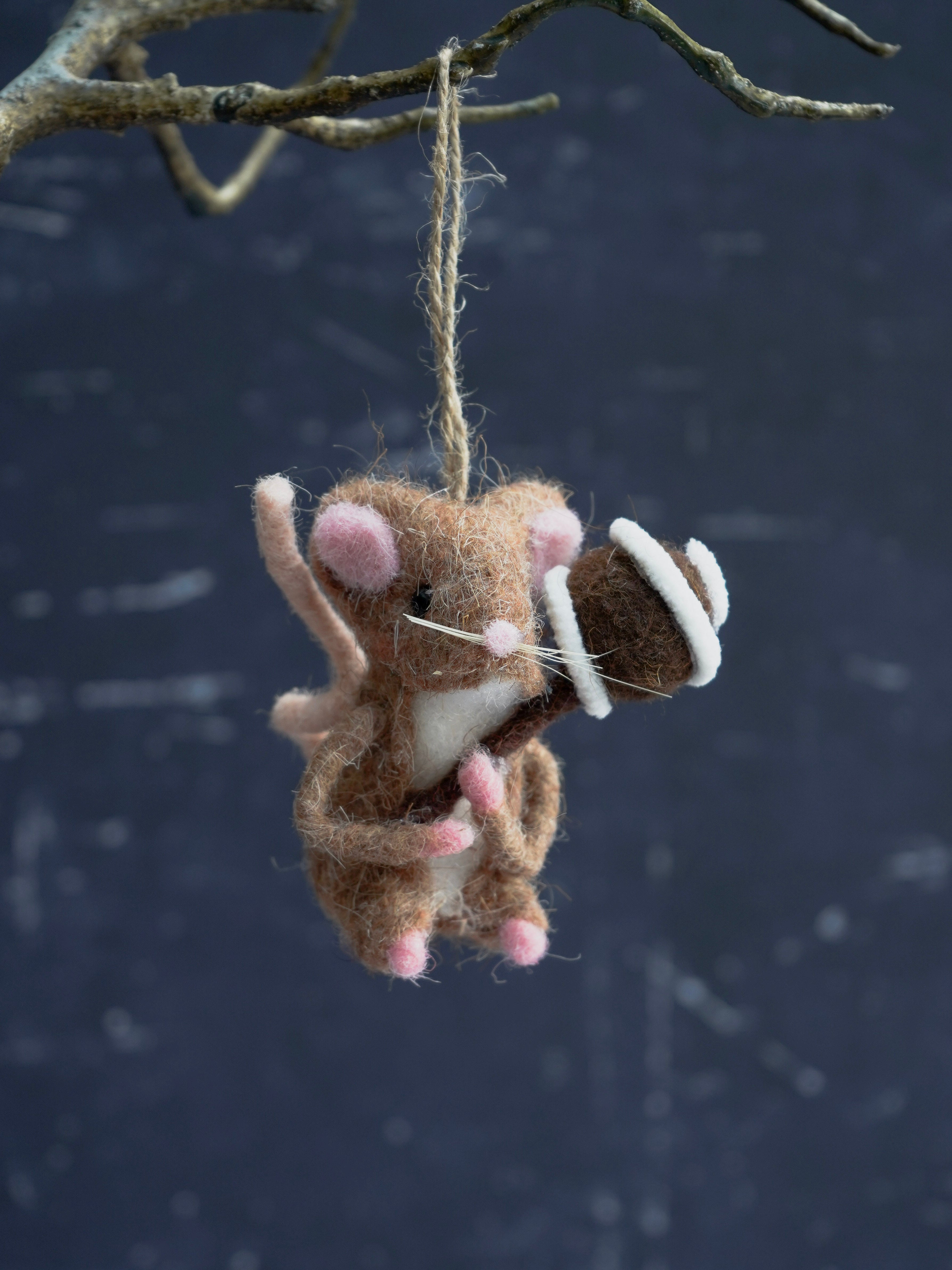 Felted mouse ornament hanging from a branch against a dark background