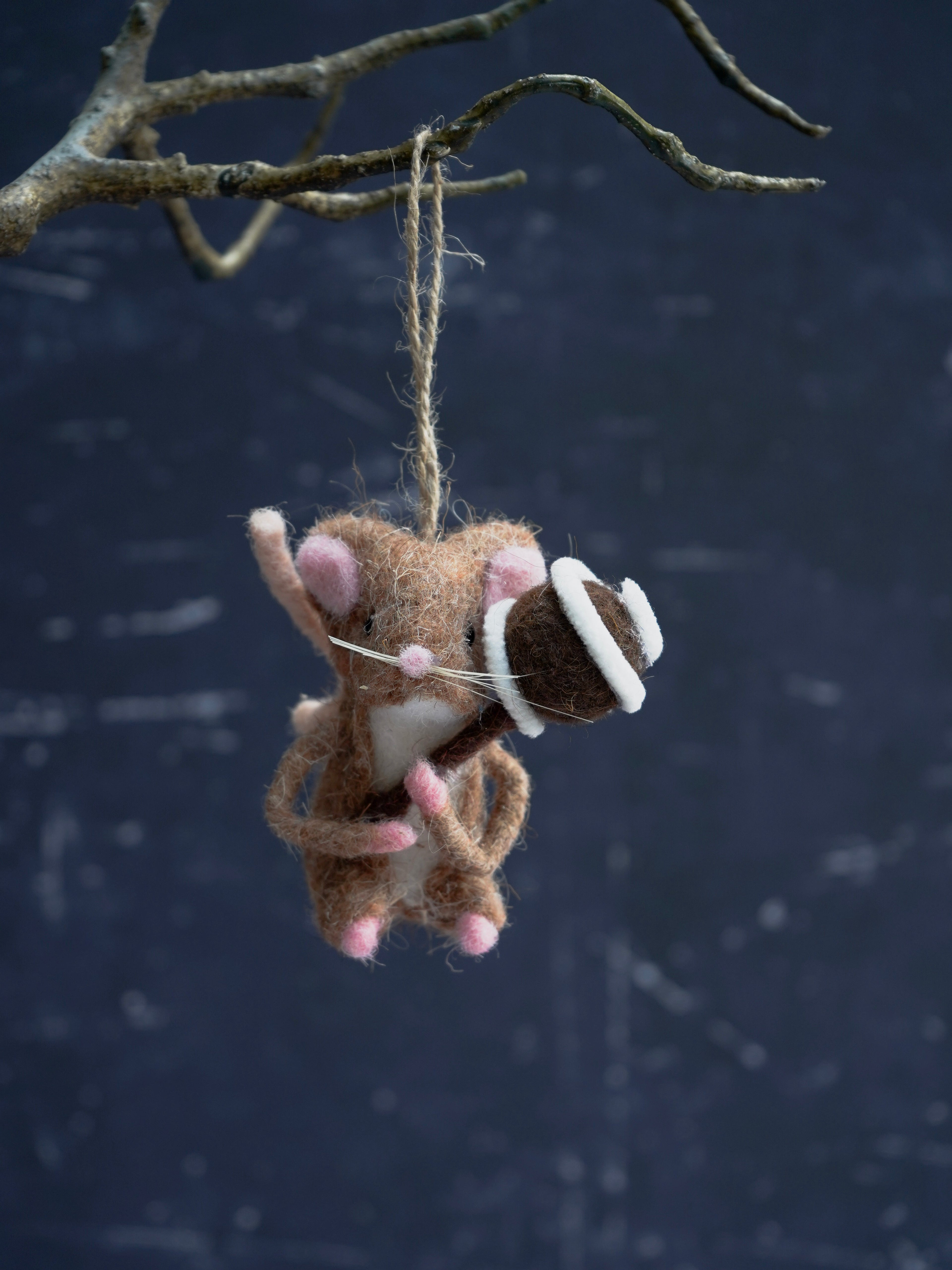 Plush toy mouse with a bow tie hanging from a branch against a dark background