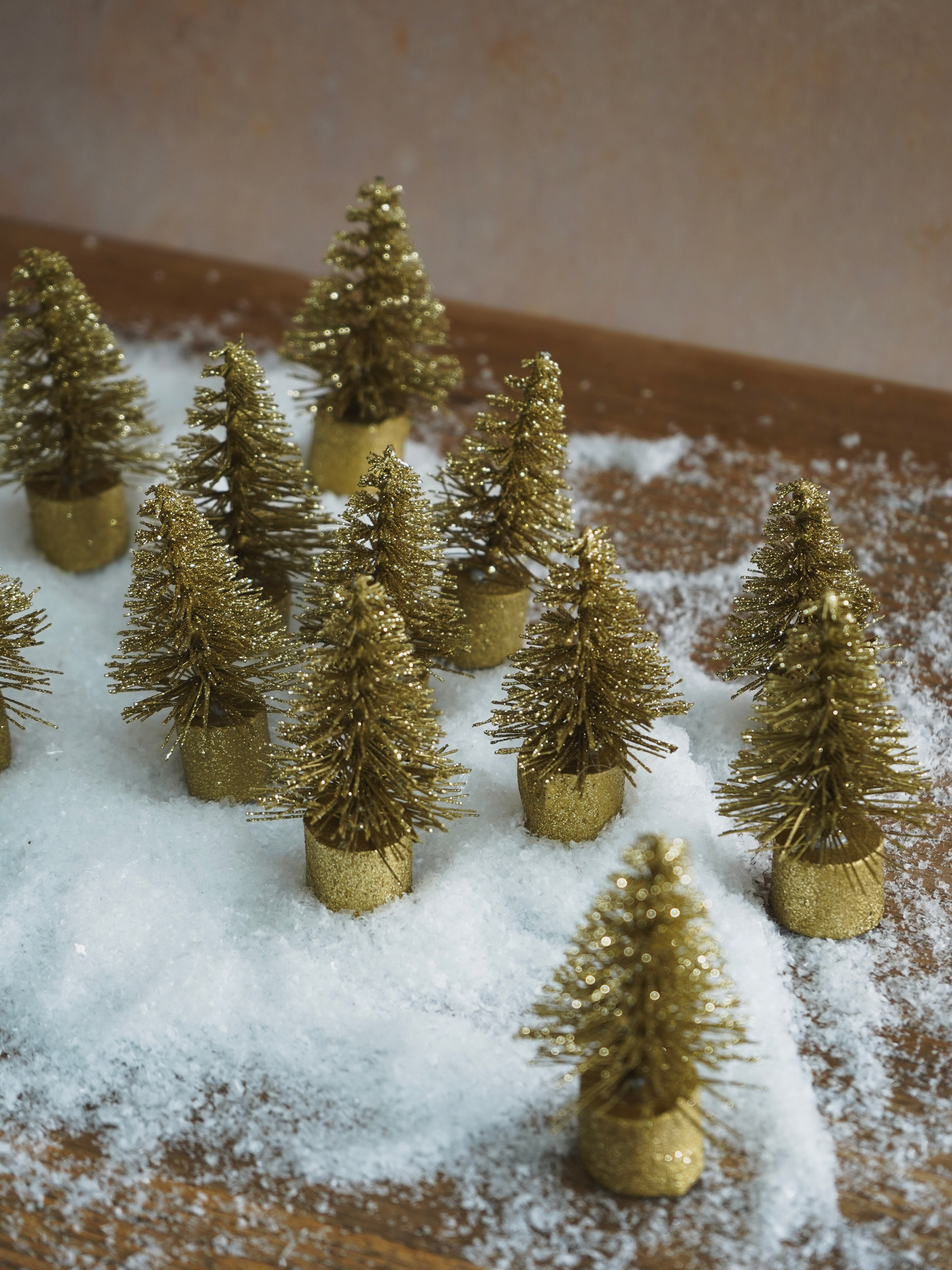 Gold and green miniature Christmas trees on a snowy surface