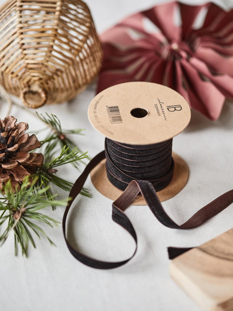 Spool of mocca brown velvet ribbon with decorative items on a light surface