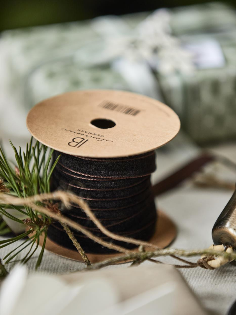Spool of mocca brown velvet ribbon with a cardboard label on a white surface with greenery.