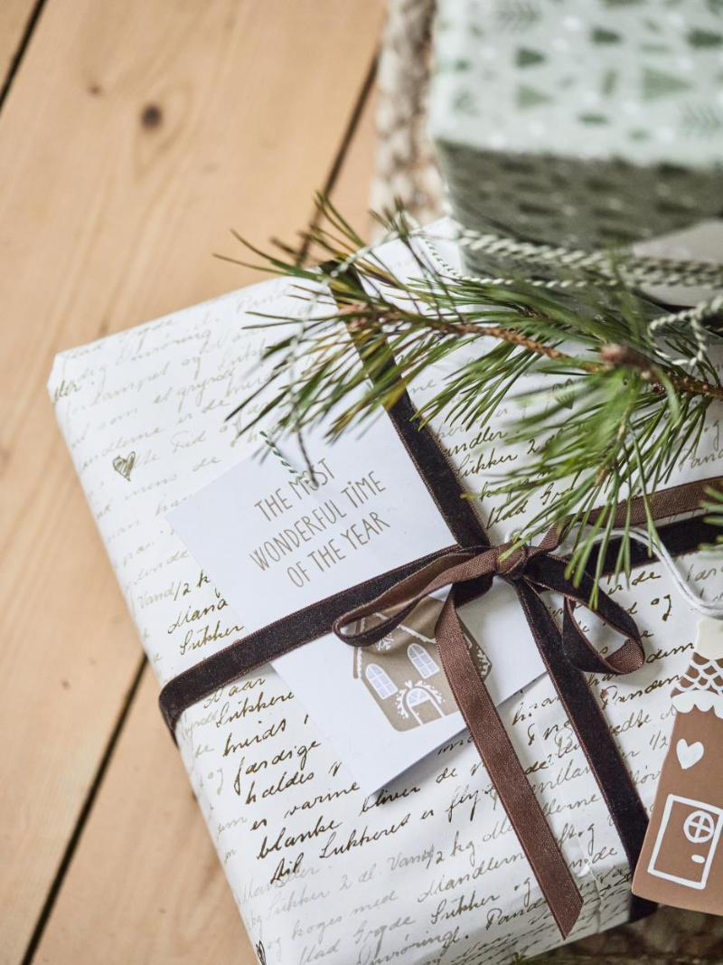 Gift wrapped in paper with text and a pine branch on a wooden surface