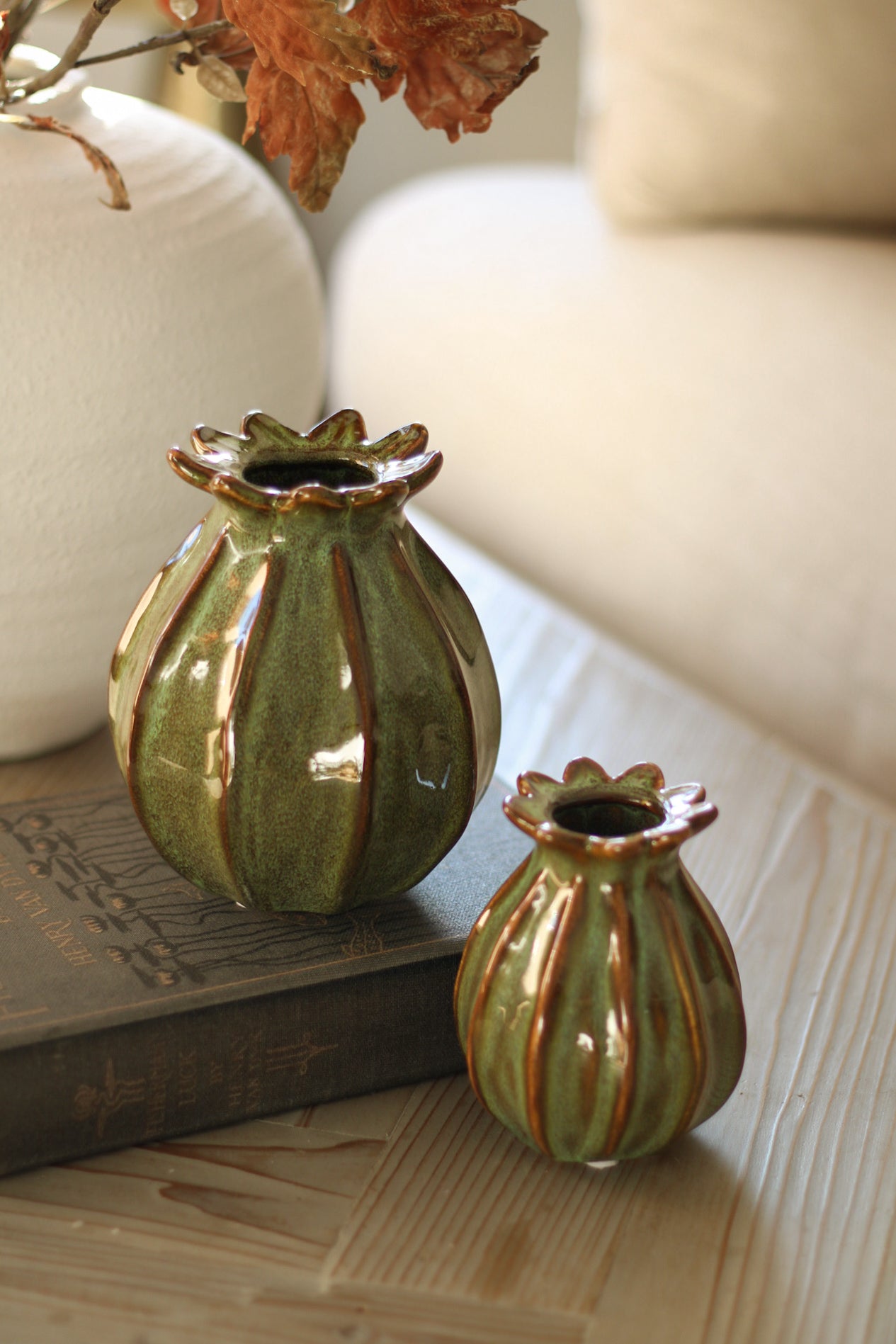 Two green ceramic poppy head vases with brown stripes on a wooden surface.