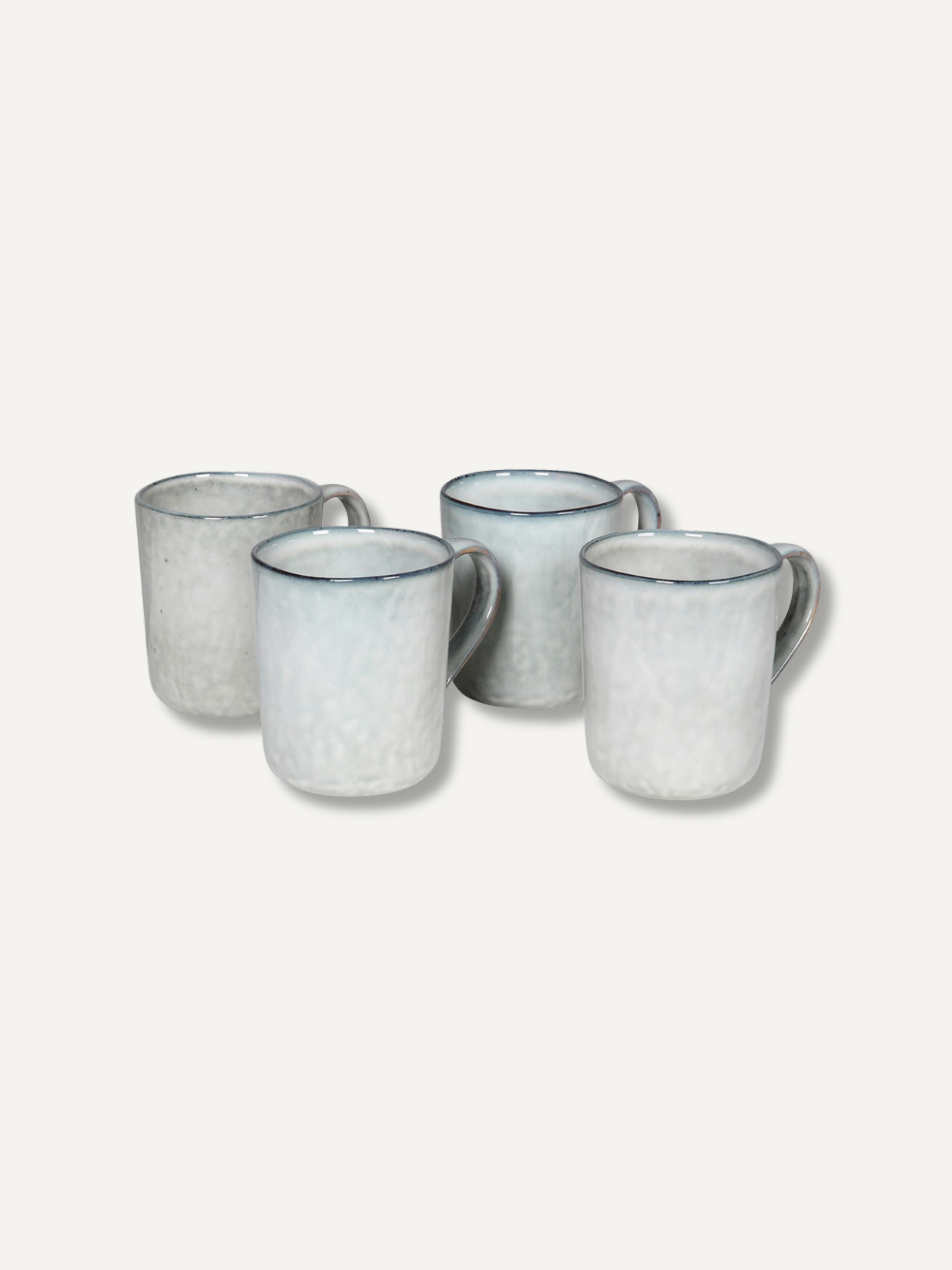 Four ceramic mugs with a speckled off-white glaze and a thin dark blue rim, arranged on a light beige background.