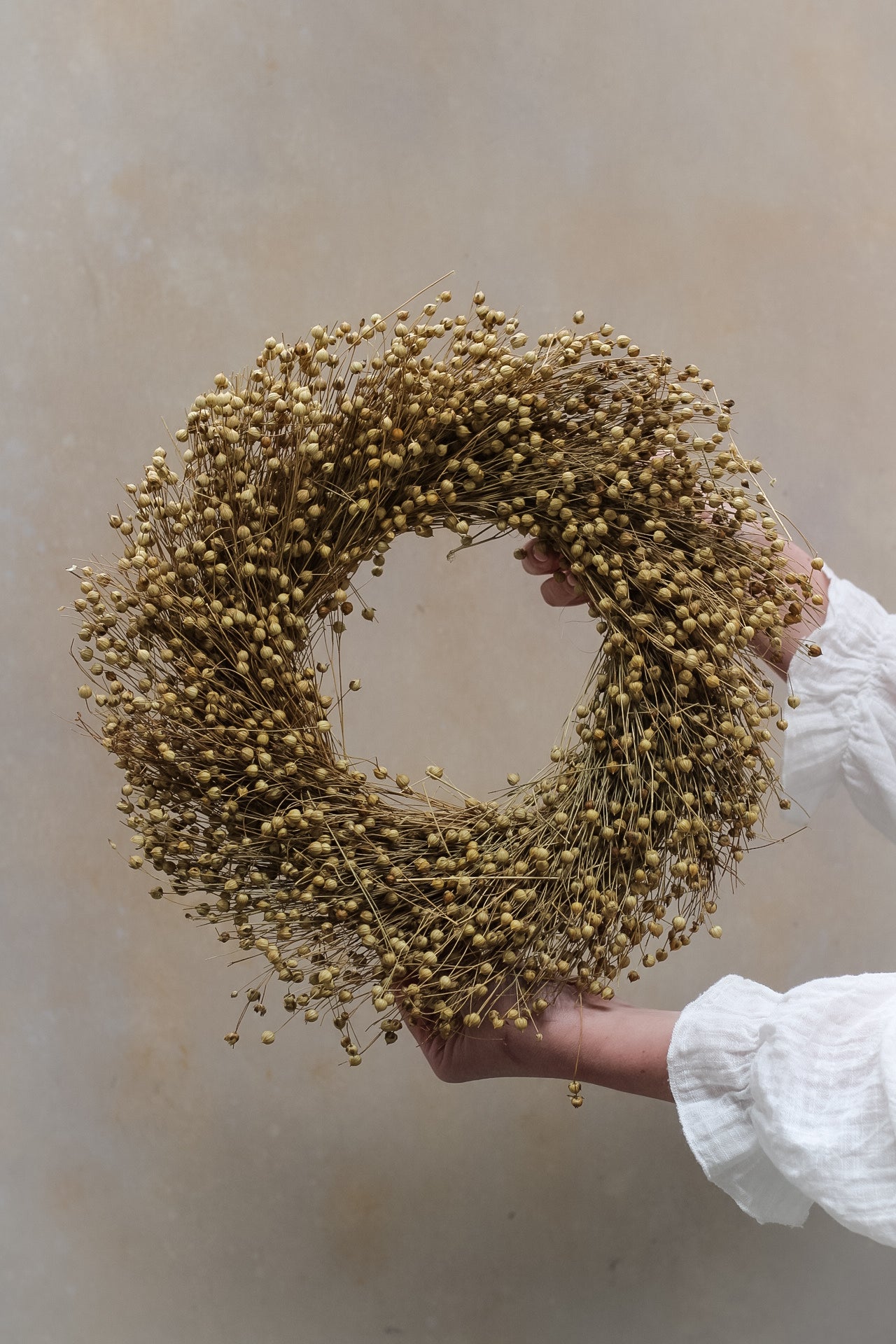 A person holding a round wreath made of natural dried flax.