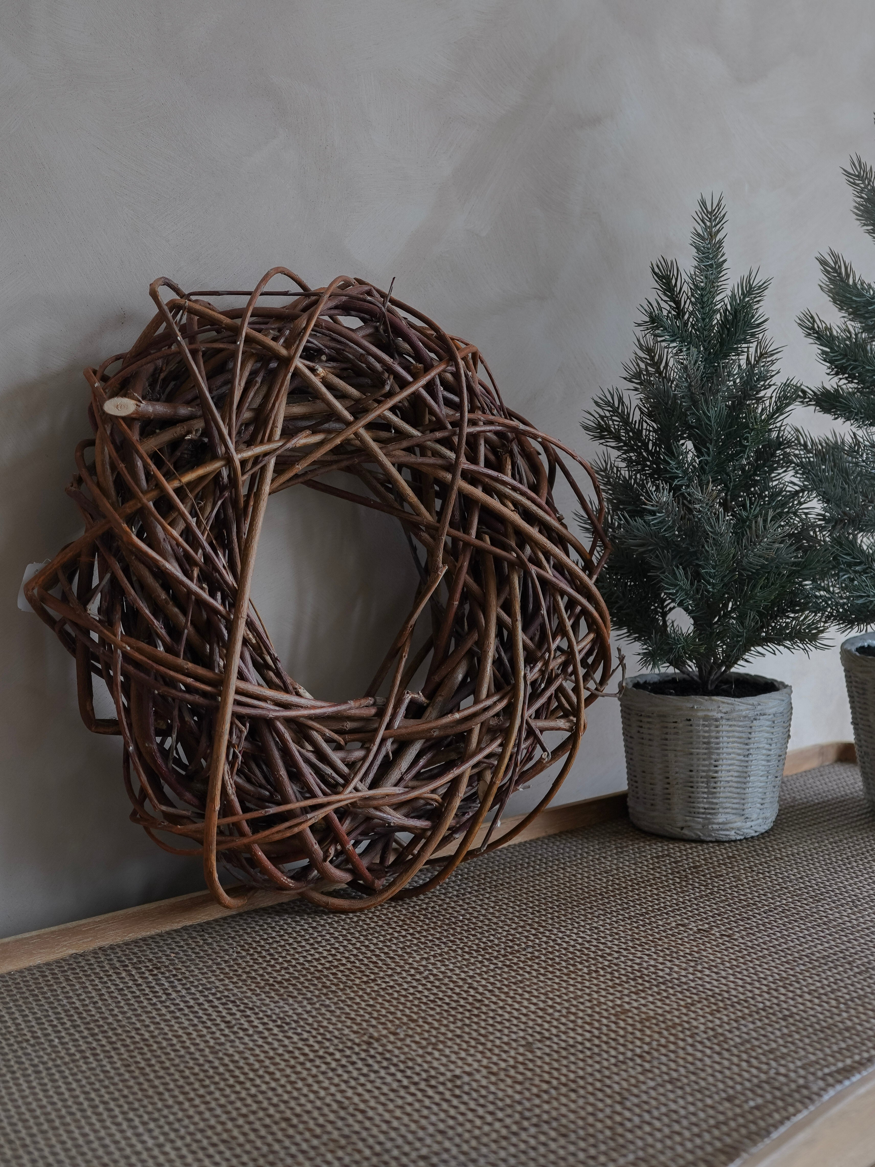 Woven decorative wreath and potted plants against a neutral wall.