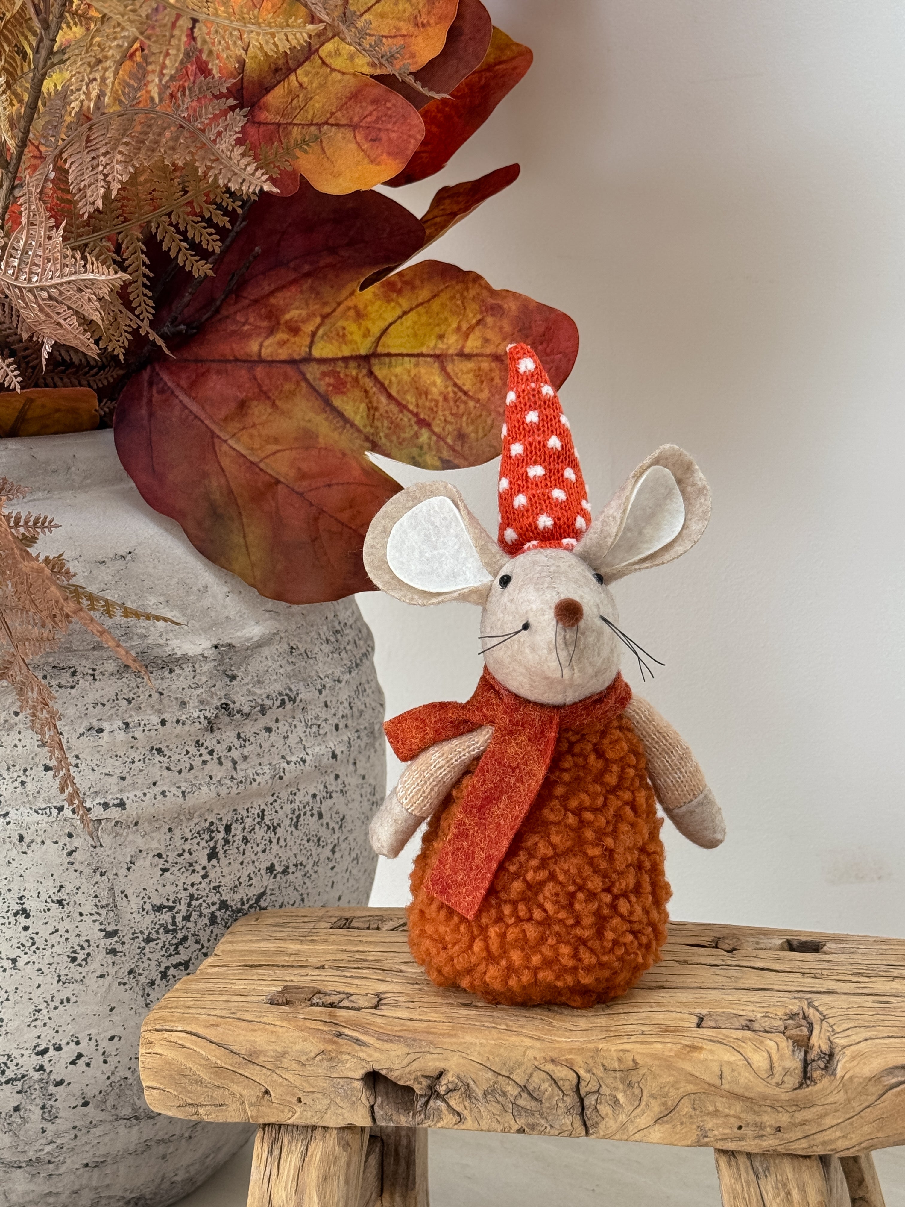 Autumn orange mouse with a red scarf and white polka dot hat on a wooden surface with leaves.