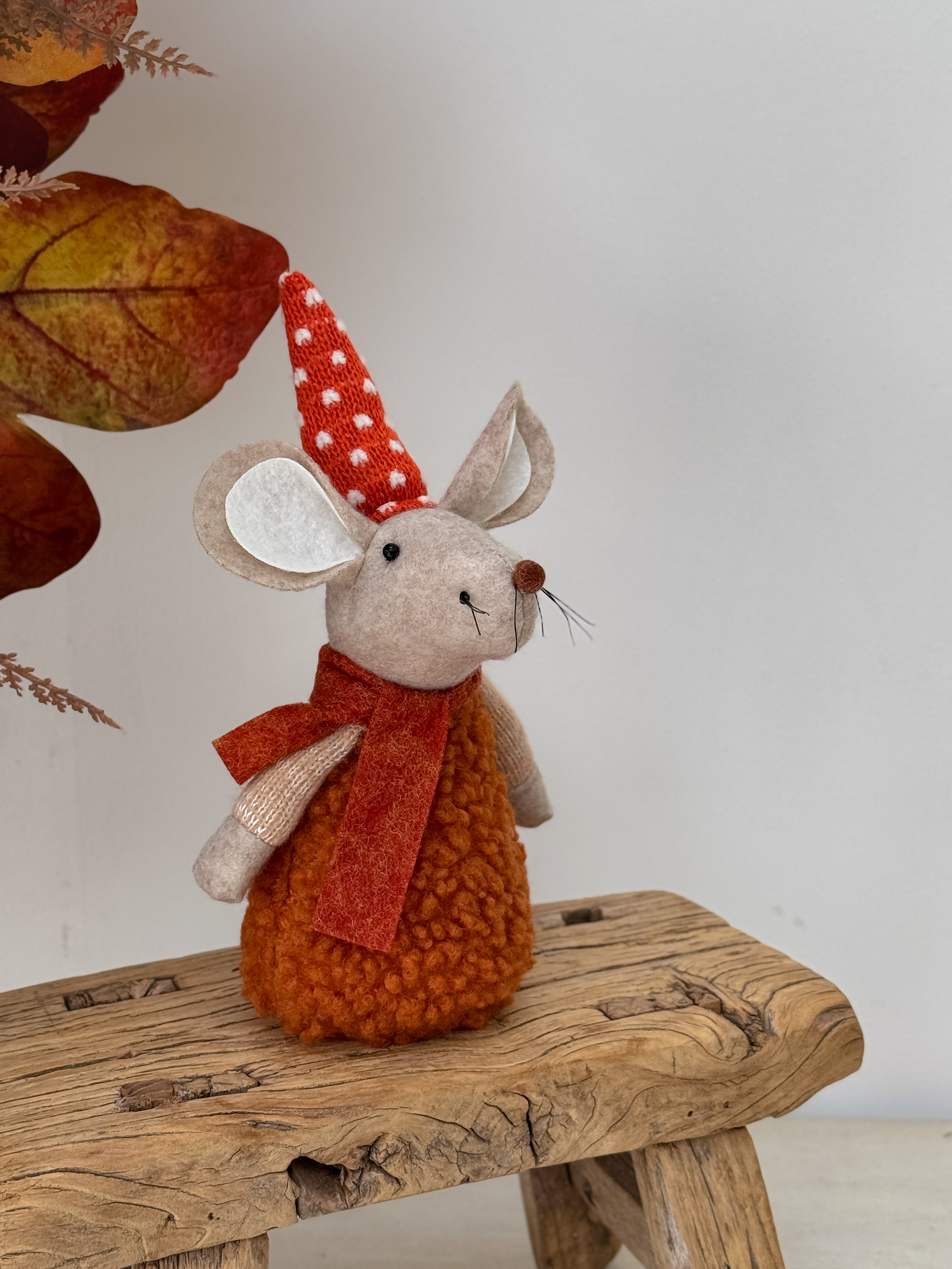 Autumn mouse decoration with a red scarf and hat on a wooden surface with autumn leaves.