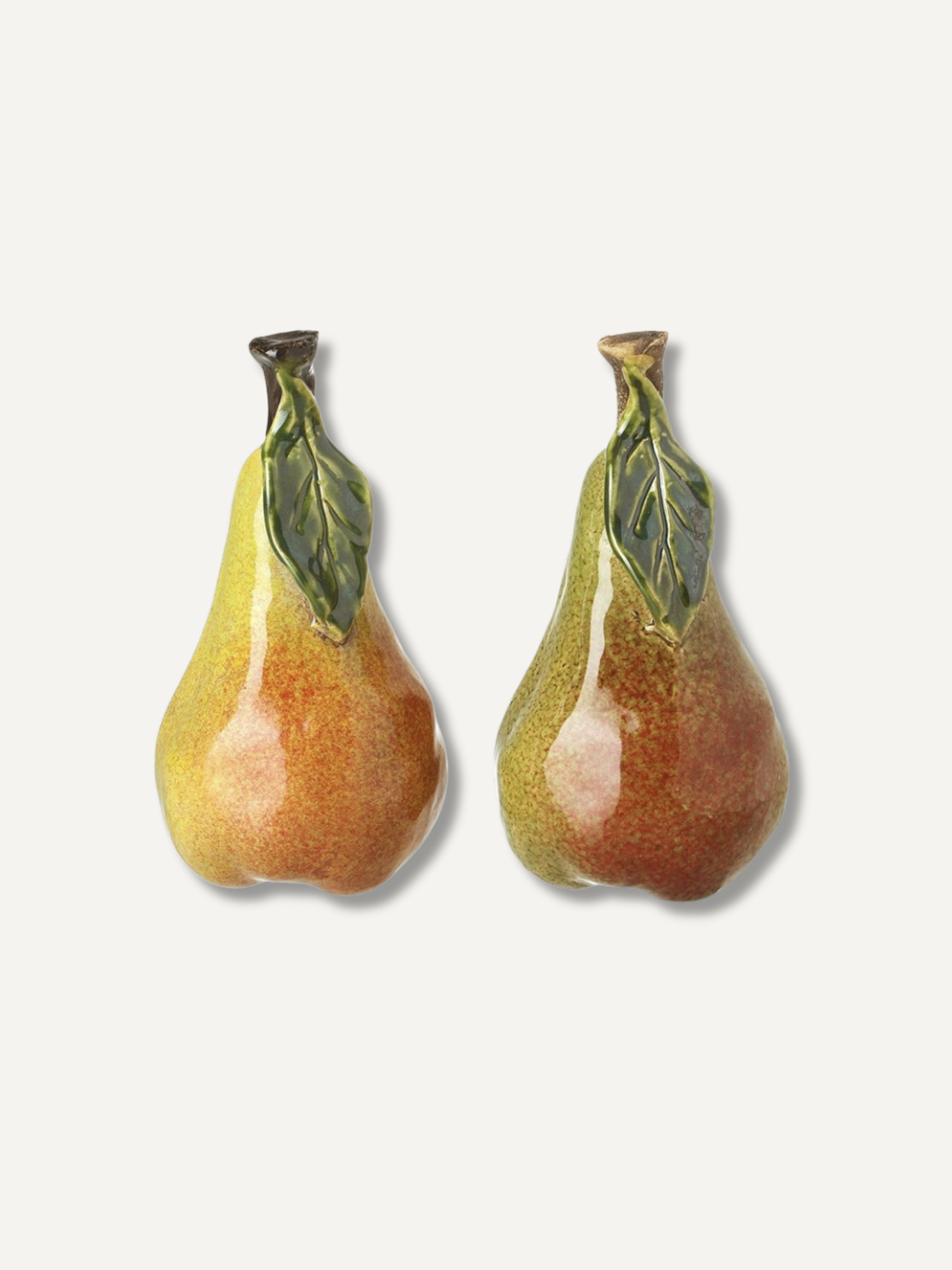 Two pear-shaped ceramic autumn ornaments with green leaves and brown stems, shown on a light off-white background.