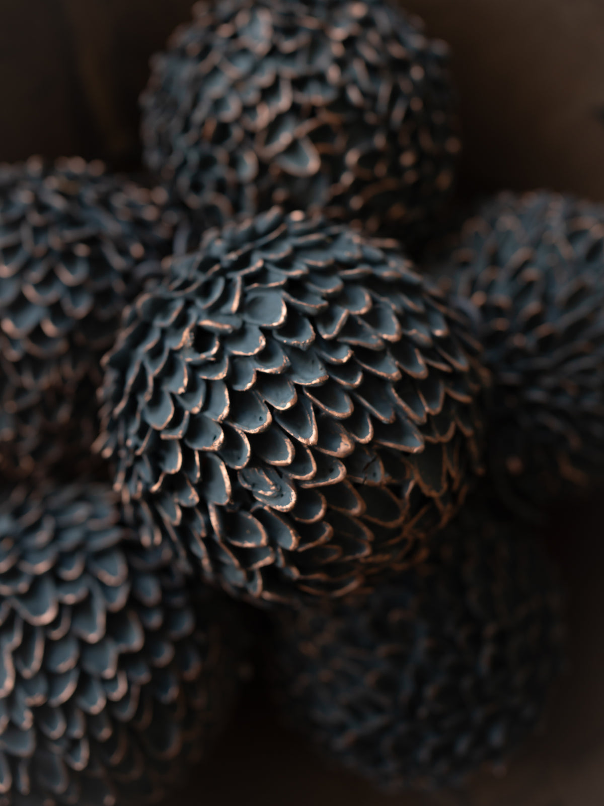 A close-up of several dark, textured decorative spheres with a pine cone pattern, photographed in low light against a dark background.