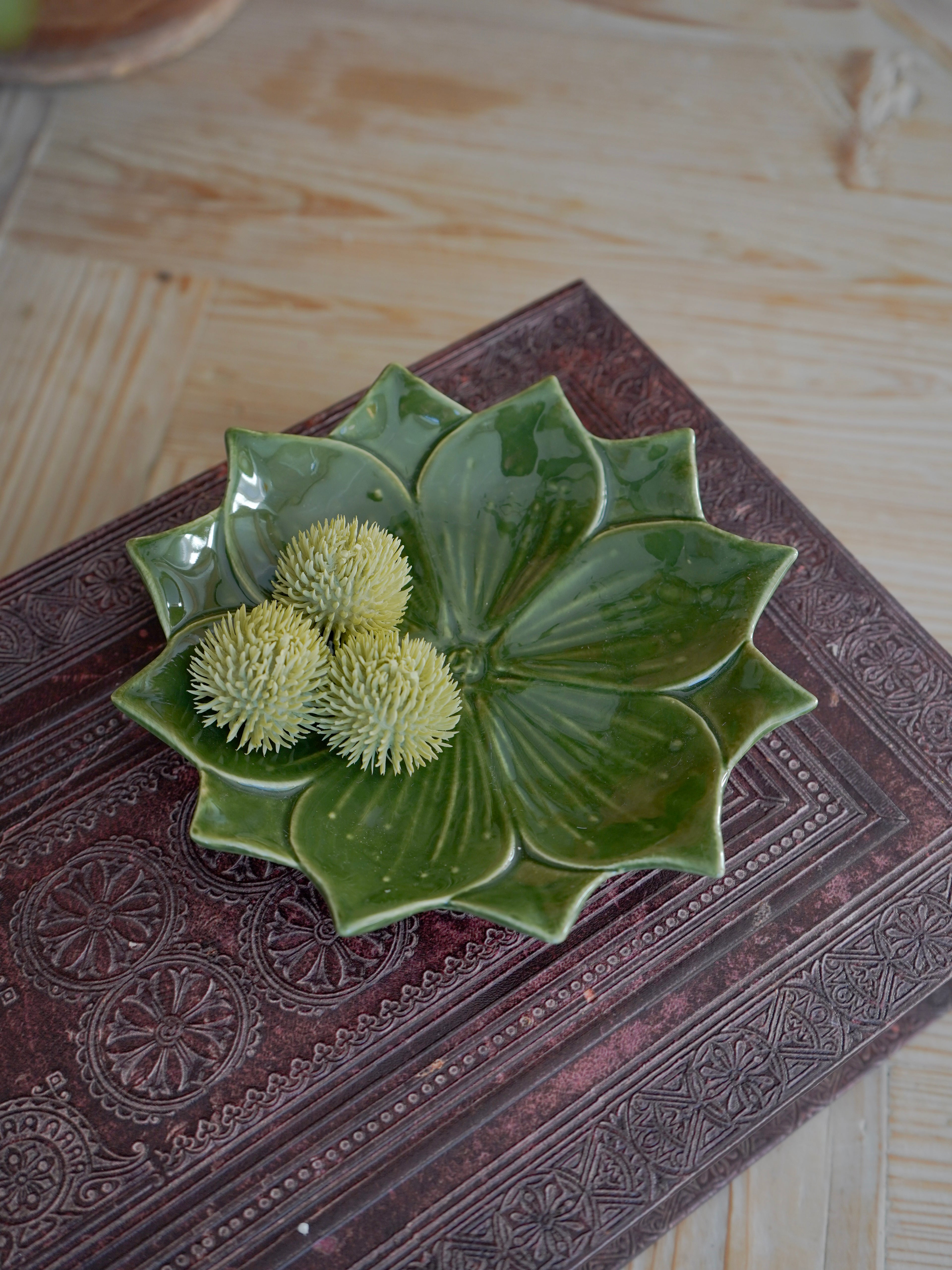 Green ceramic flower-shaped trinket dish with decorative elements on a textured surface