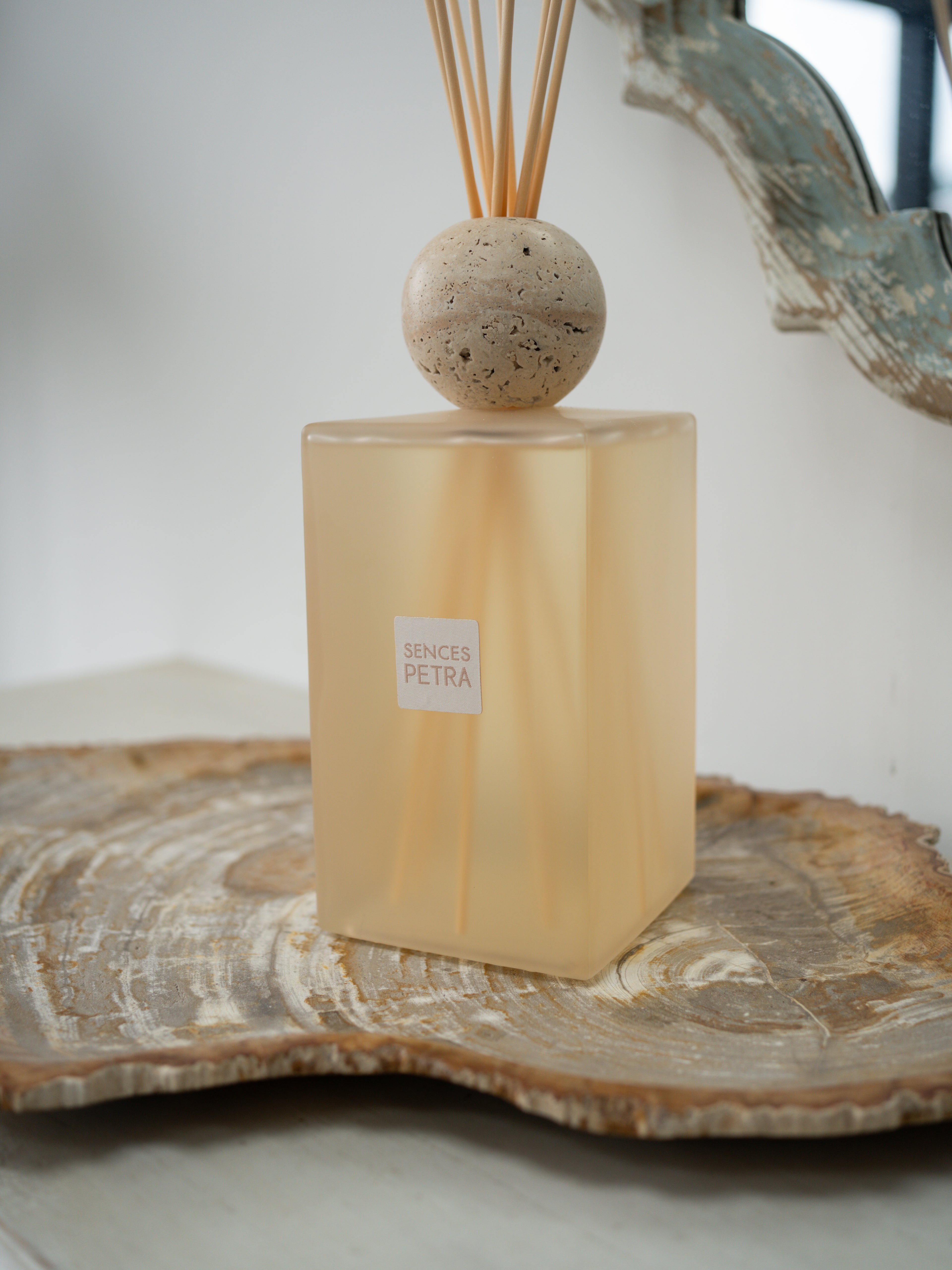 A extra large petra reed diffuser bottle in frosted warm beige glass with a round stone top and natural reed sticks, displayed on a wood slice tray against a soft neutral background.