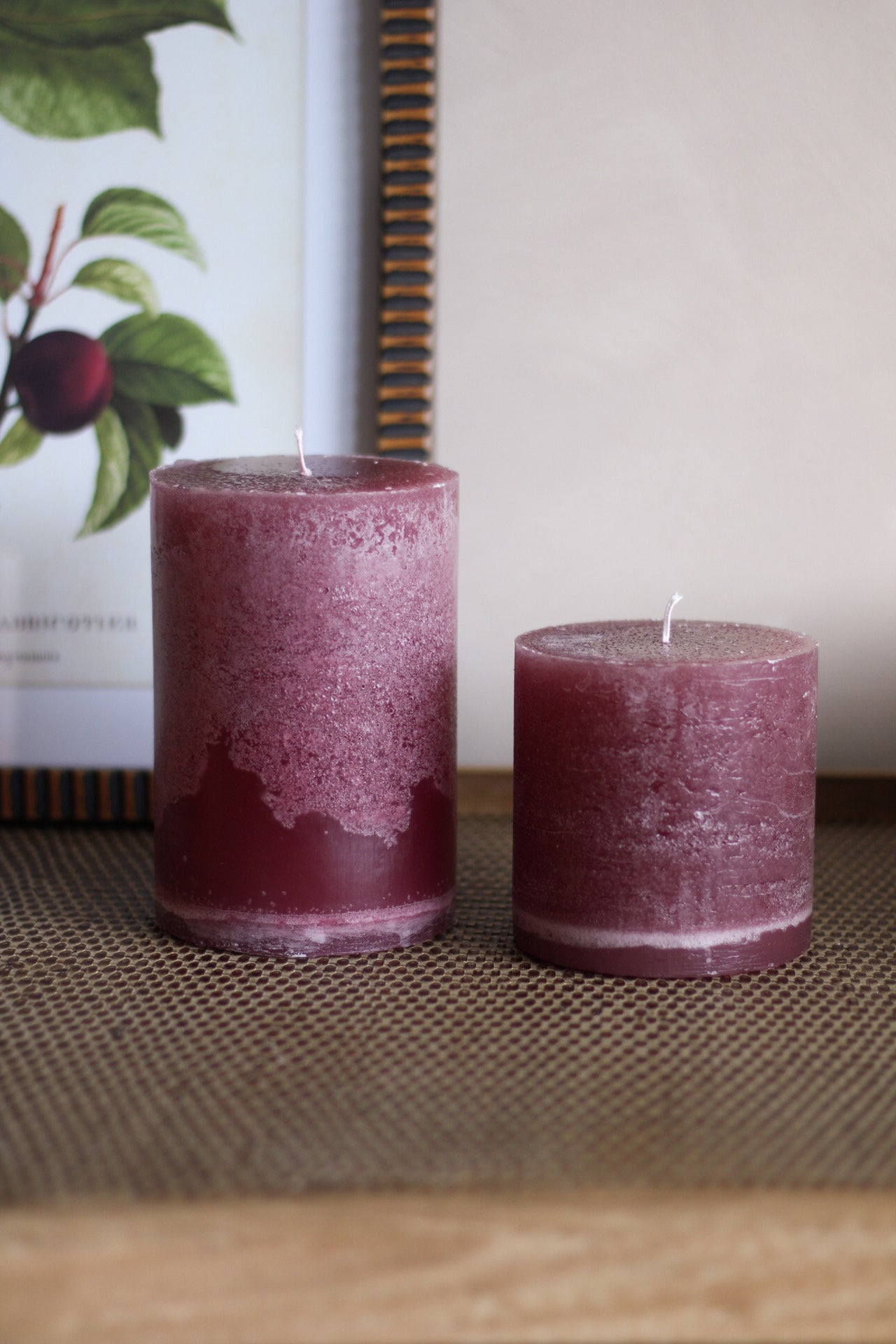Two plum candles on a textured surface with a blurred background