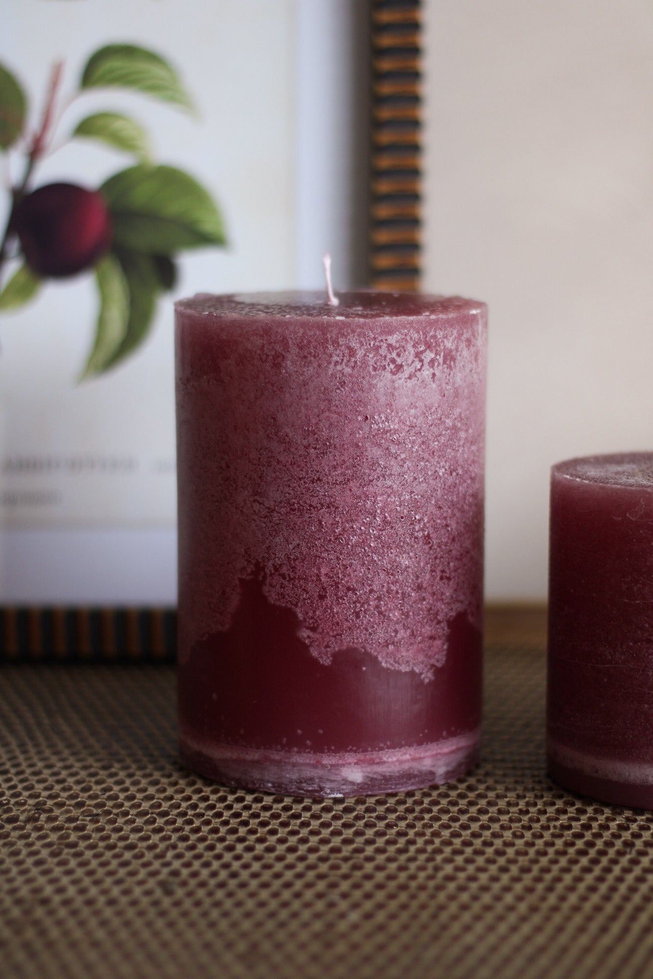 Two plum candles on a textured surface with a blurred background