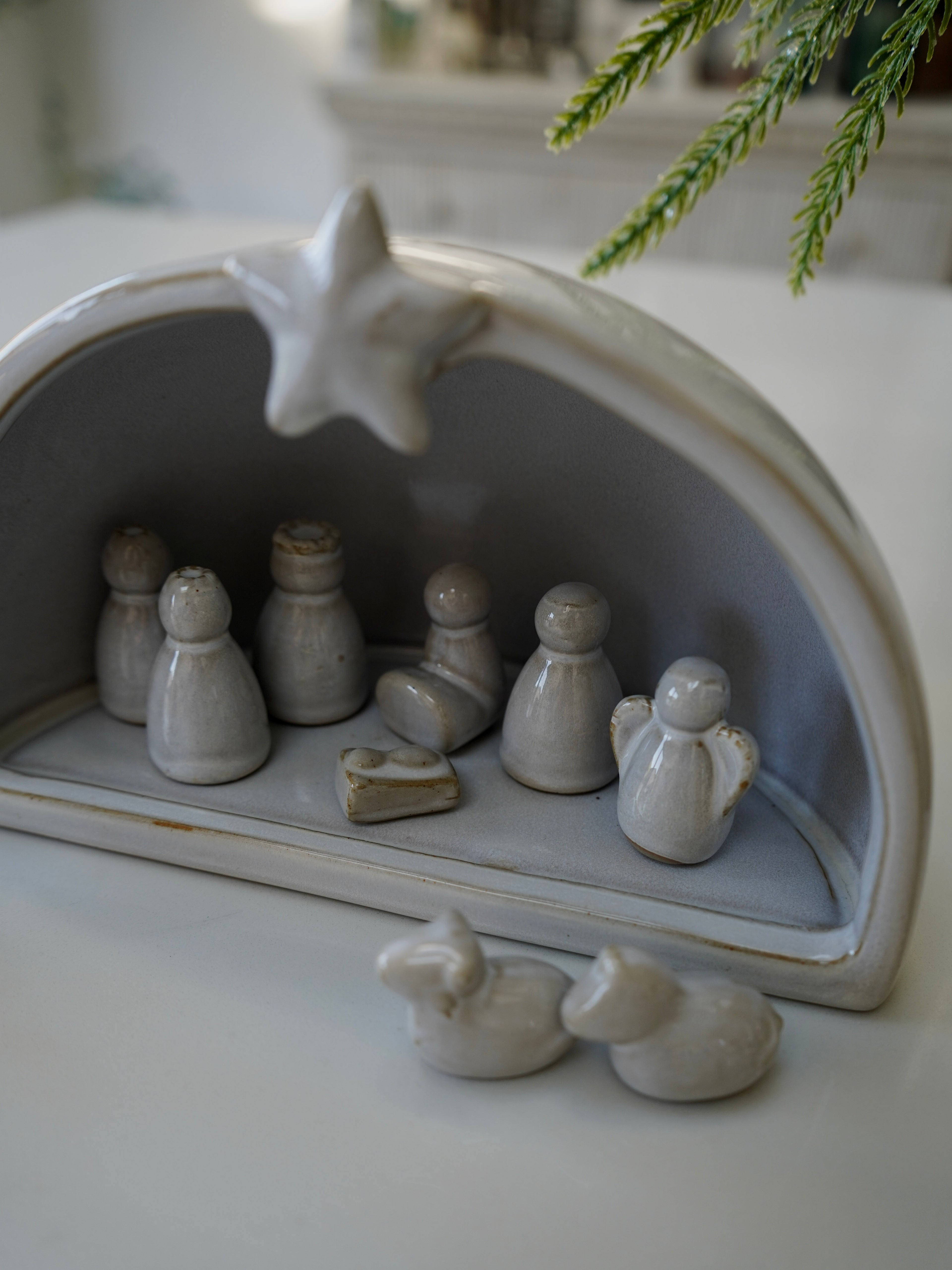 Small ceramic nativity scene with figures and a star on a white surface.