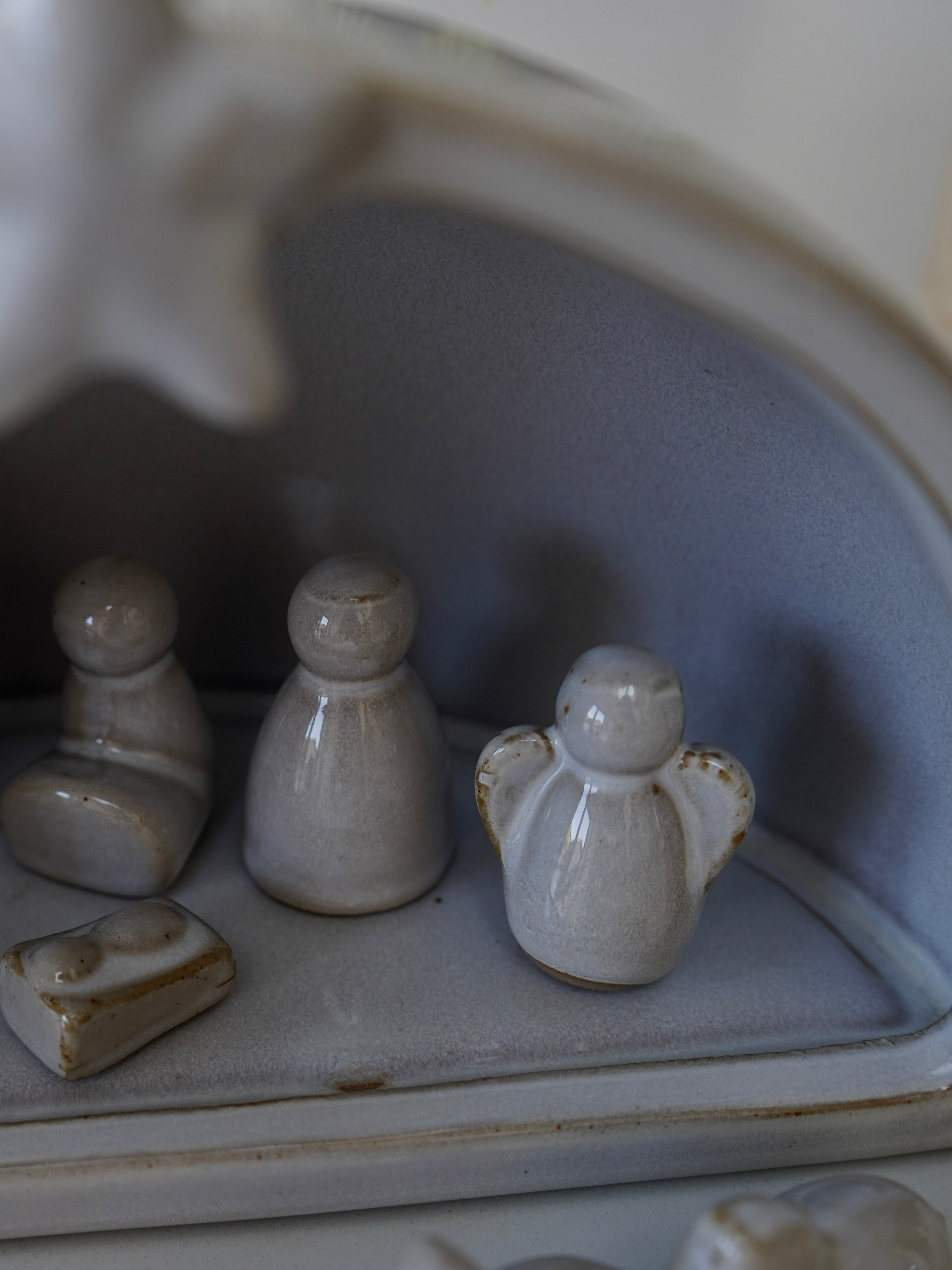 Small ceramic figures including a seated figure, standing figure, and angel on a textured surface.