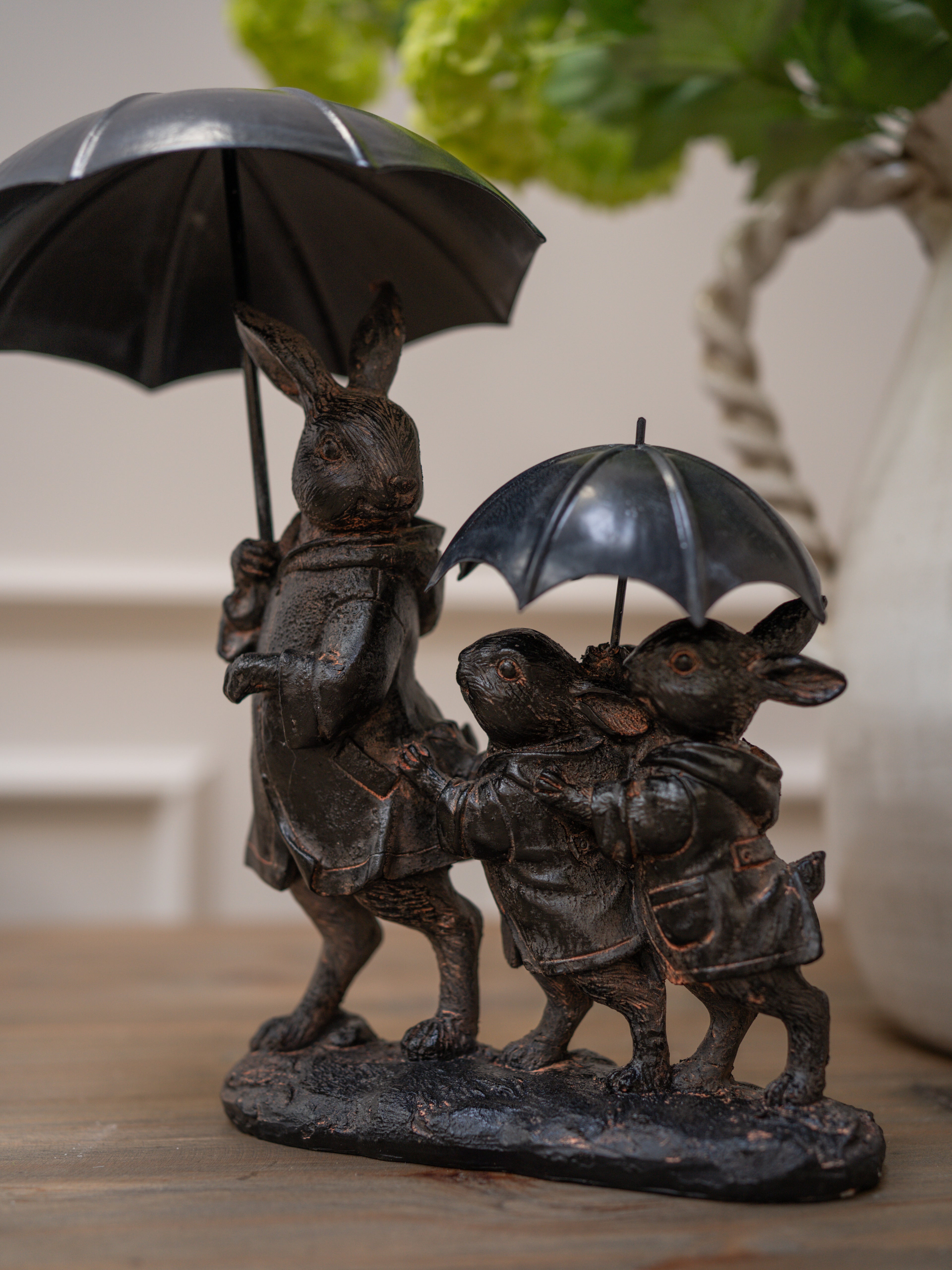 Bronze sculpture of three rabbits with umbrellas on a wooden surface