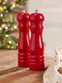 Two red salt and pepper shakers on a wooden surface with a blurred festive background.