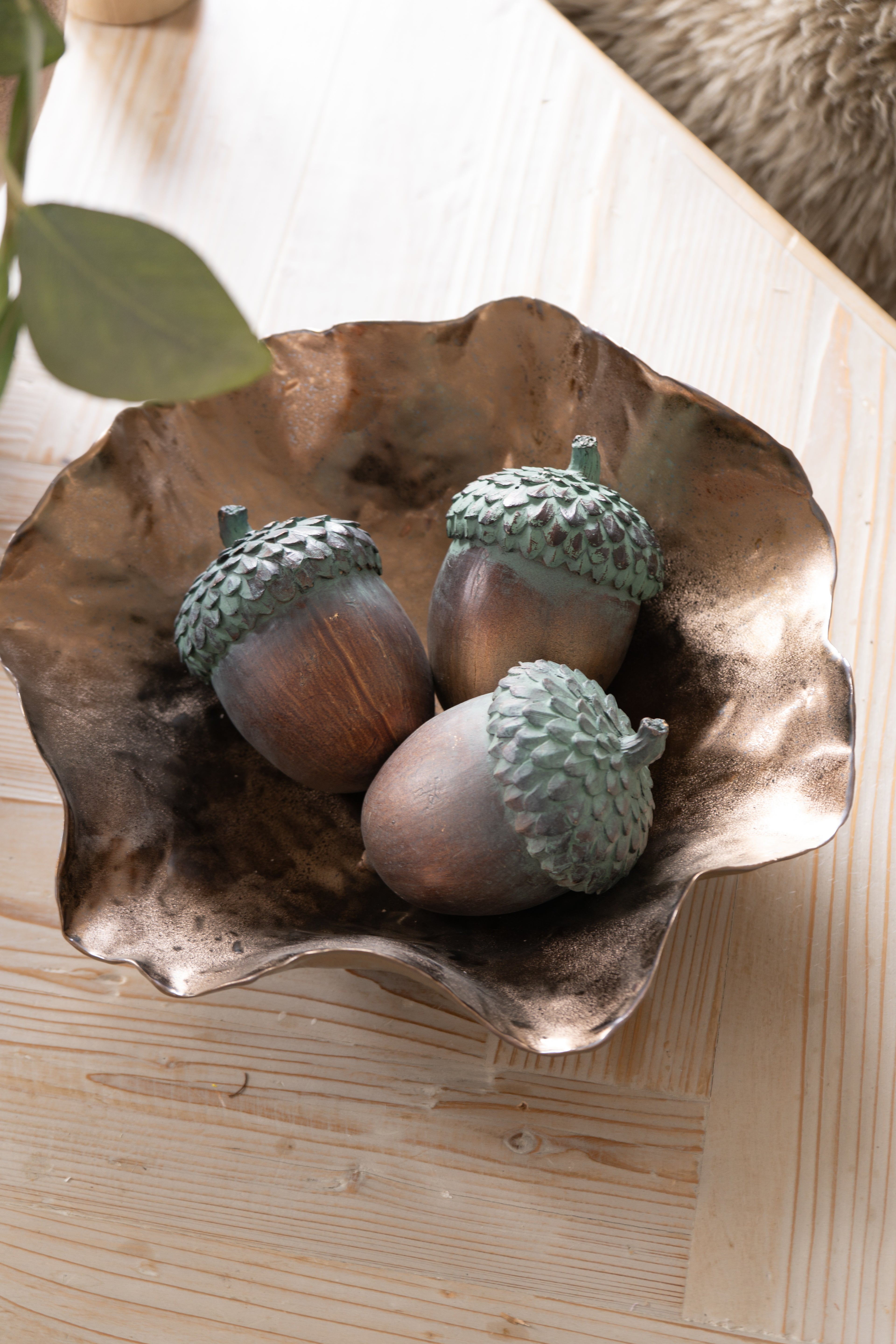 Decorative bronze bowl with acorn ornaments on a wooden surface