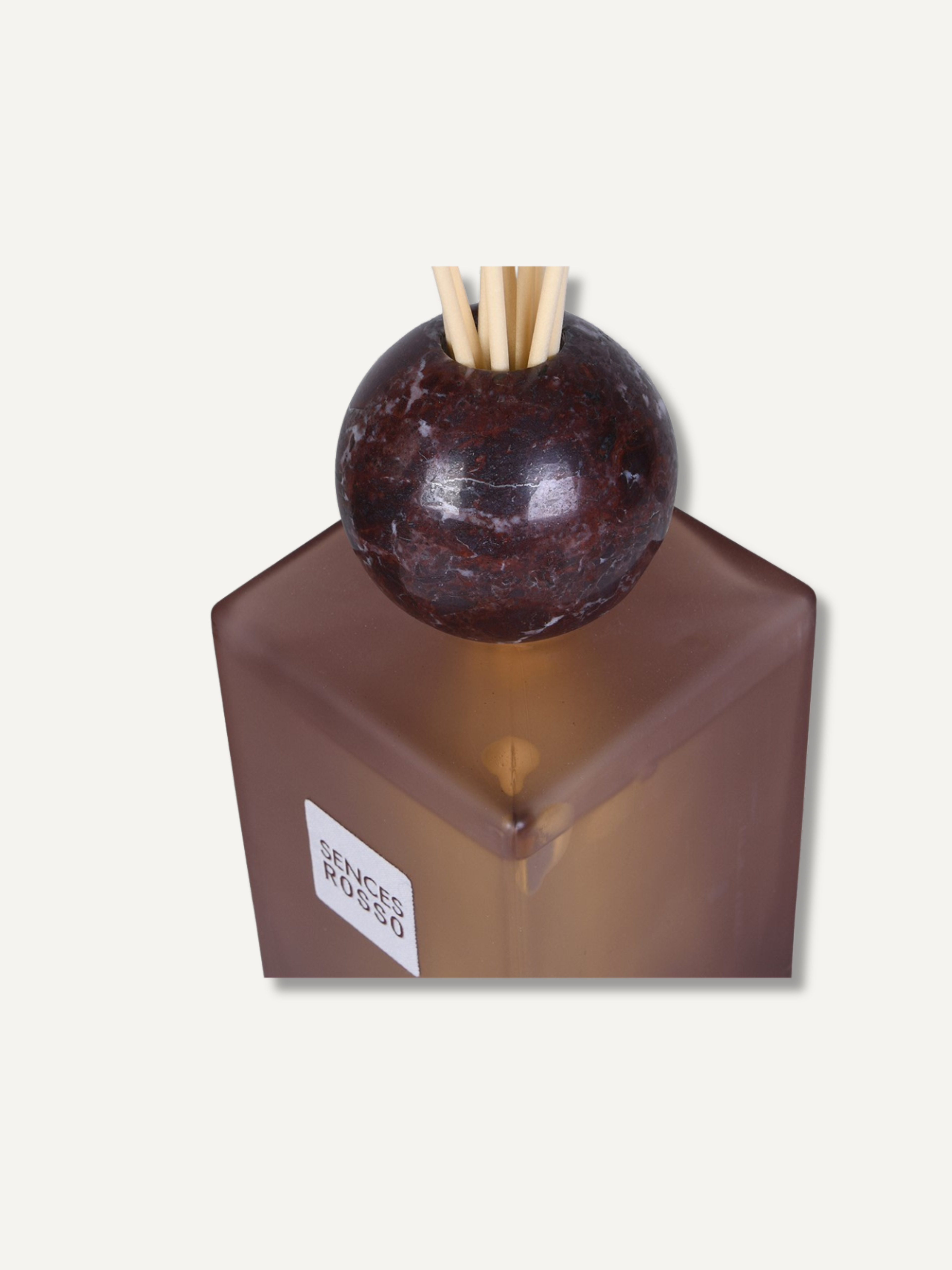 A reed diffuser bottle in a frosted translucent burgundy glass, topped with a dark polished stone sphere and natural reed sticks, shown on a light beige background.
