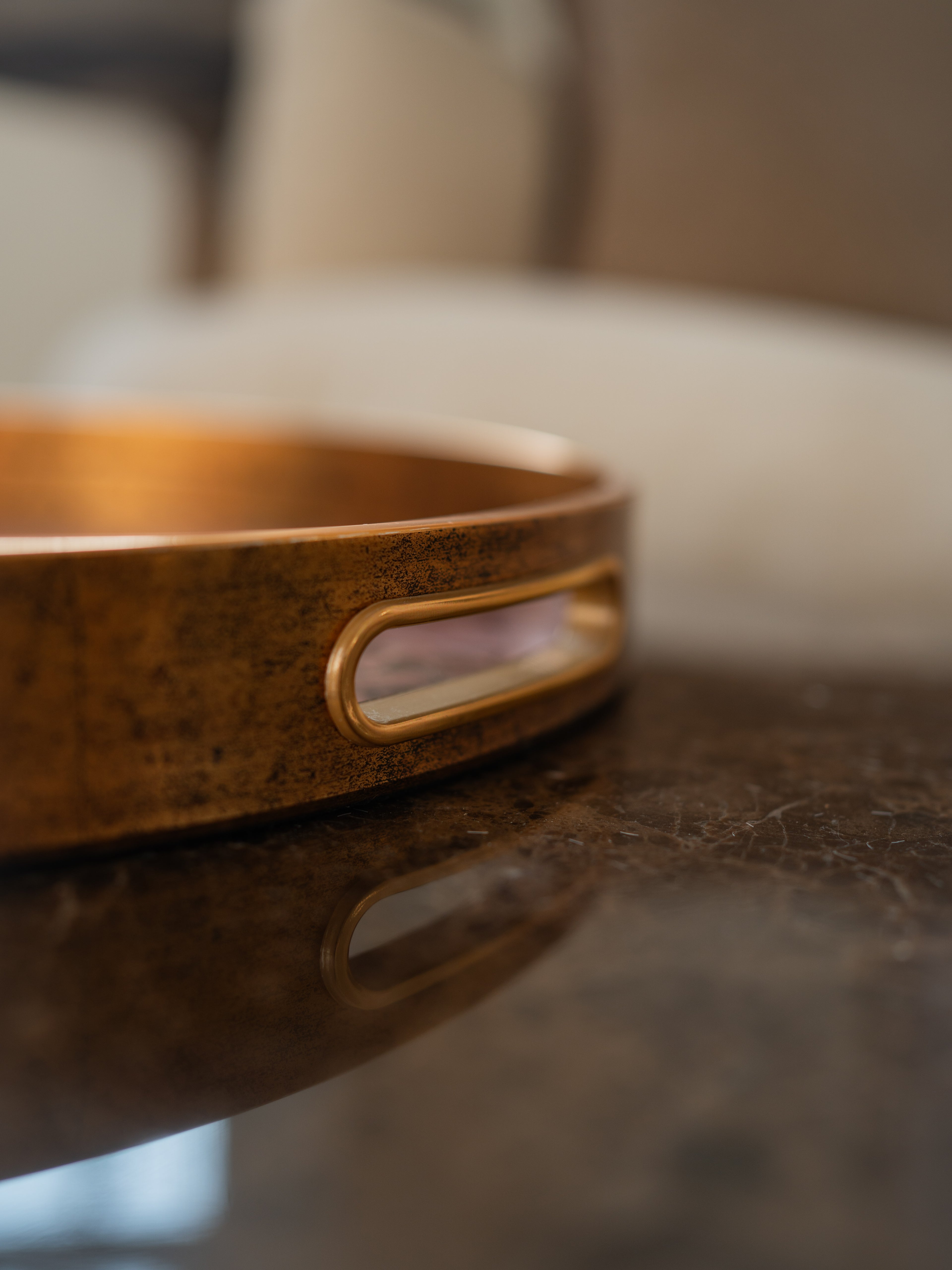A close-up of a round gold edged tray cut out handle resting on a dark reflective surface.