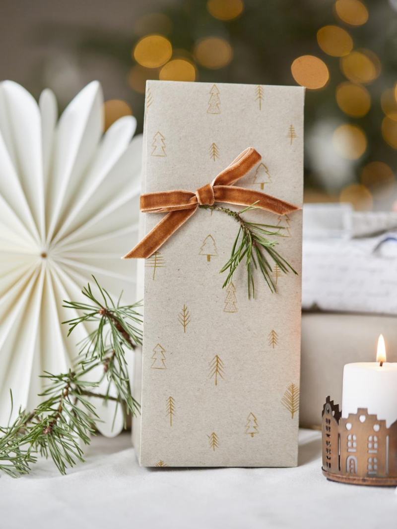 Gift box with gold tree patterns, orange ribbon, and greenery against a blurred festive background.