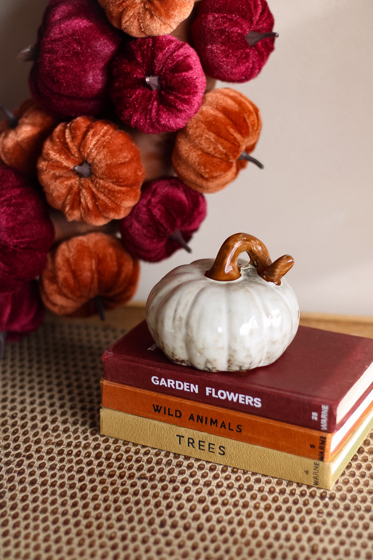 White ceramic pumpkin on books with fall-themed decor in the background