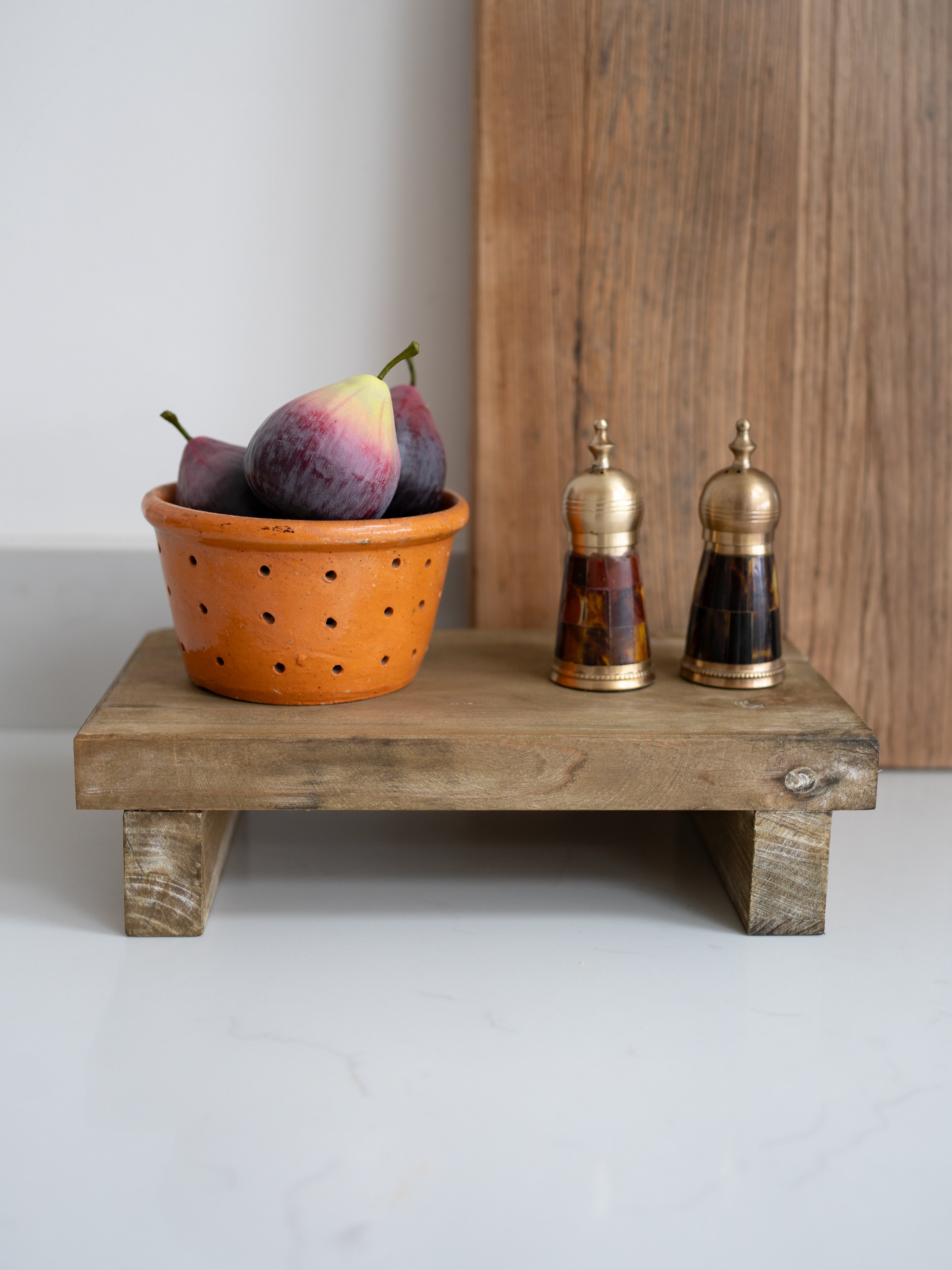 Wooden stand with a pot of fruits and two decorative bottles on a plain background
