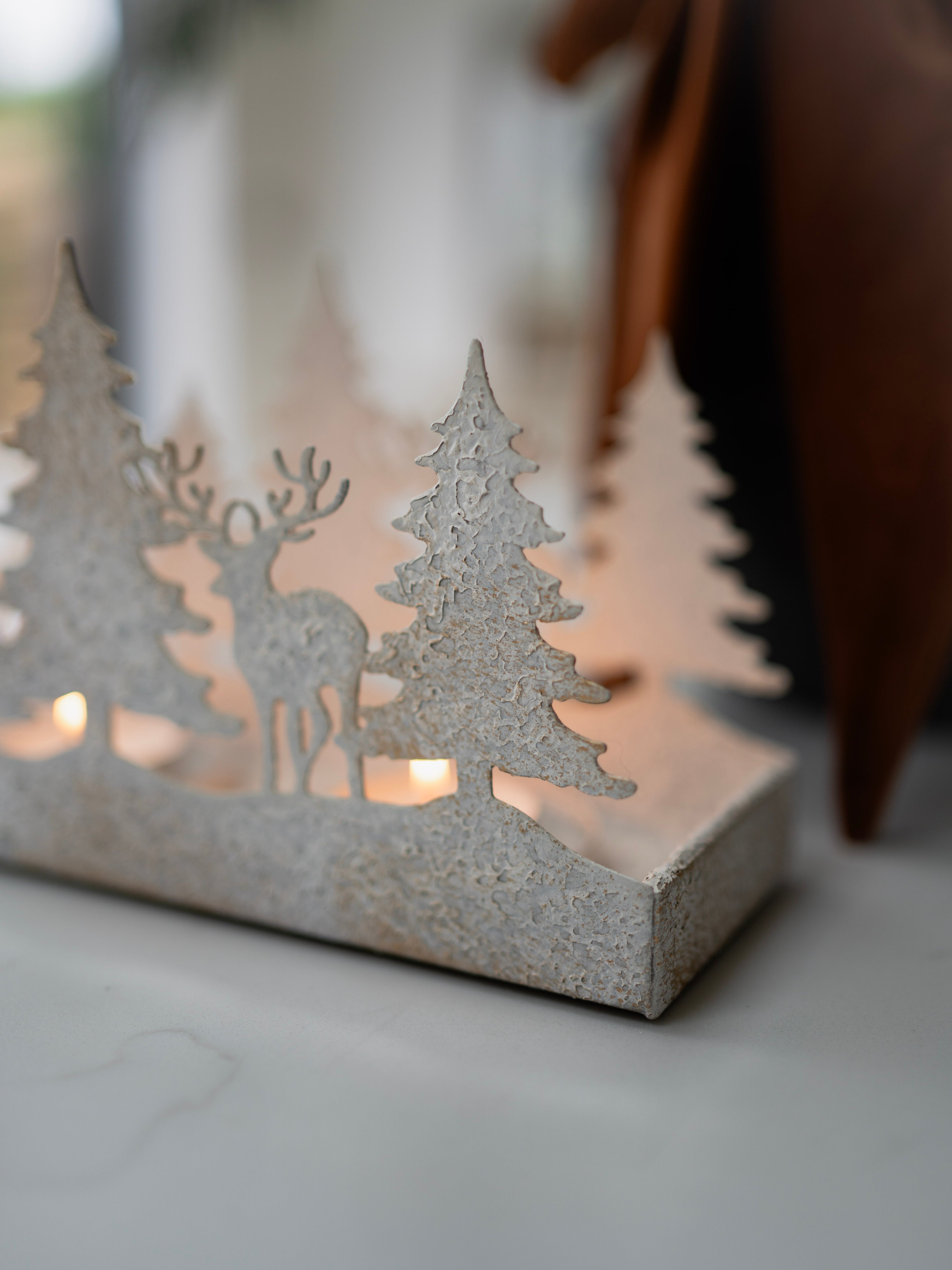 Decorative candle holder with cut-out trees and reindeer on a neutral background