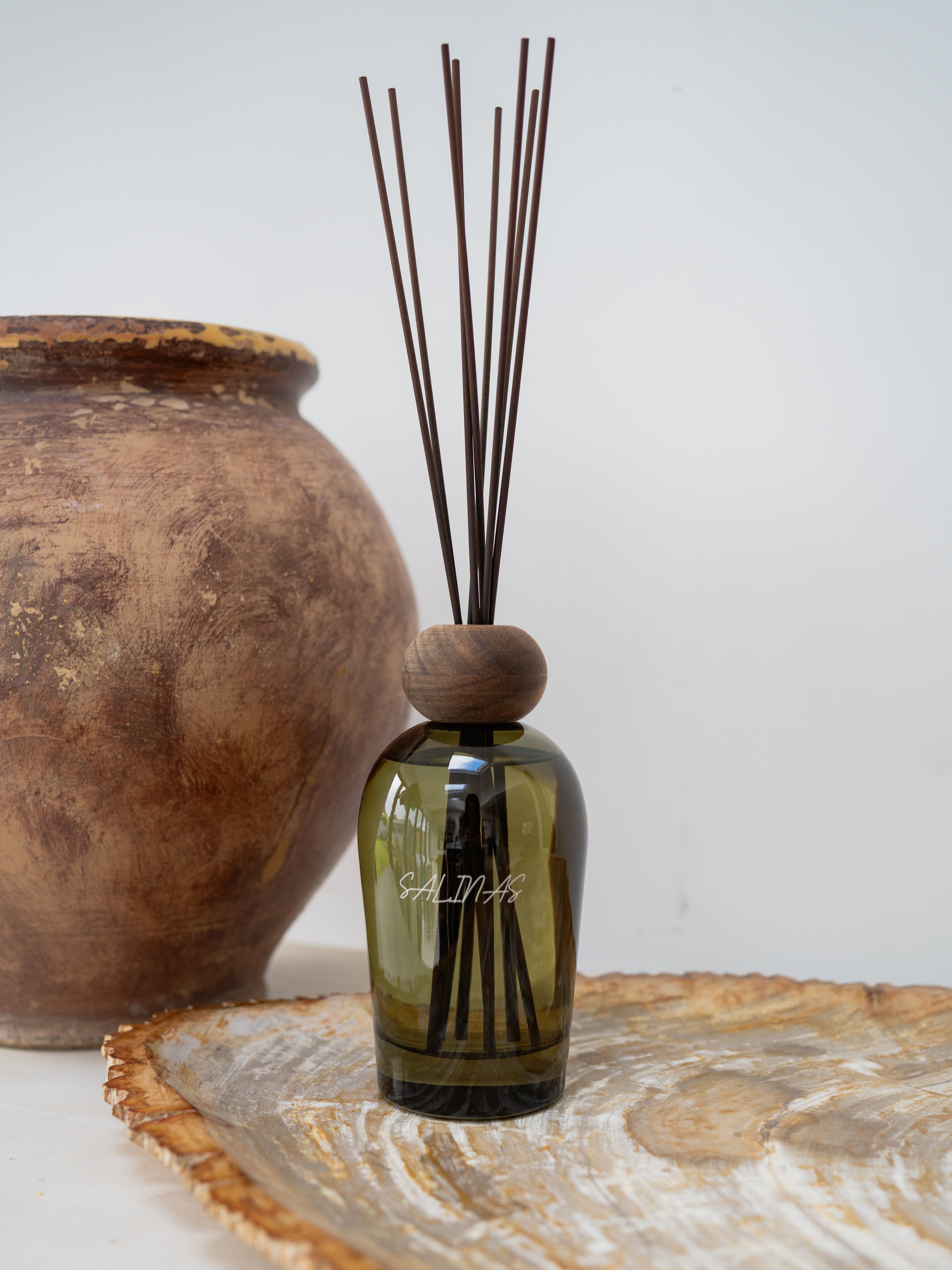A green diffuser bottle with wooden cap and sticks on a decorative surface.