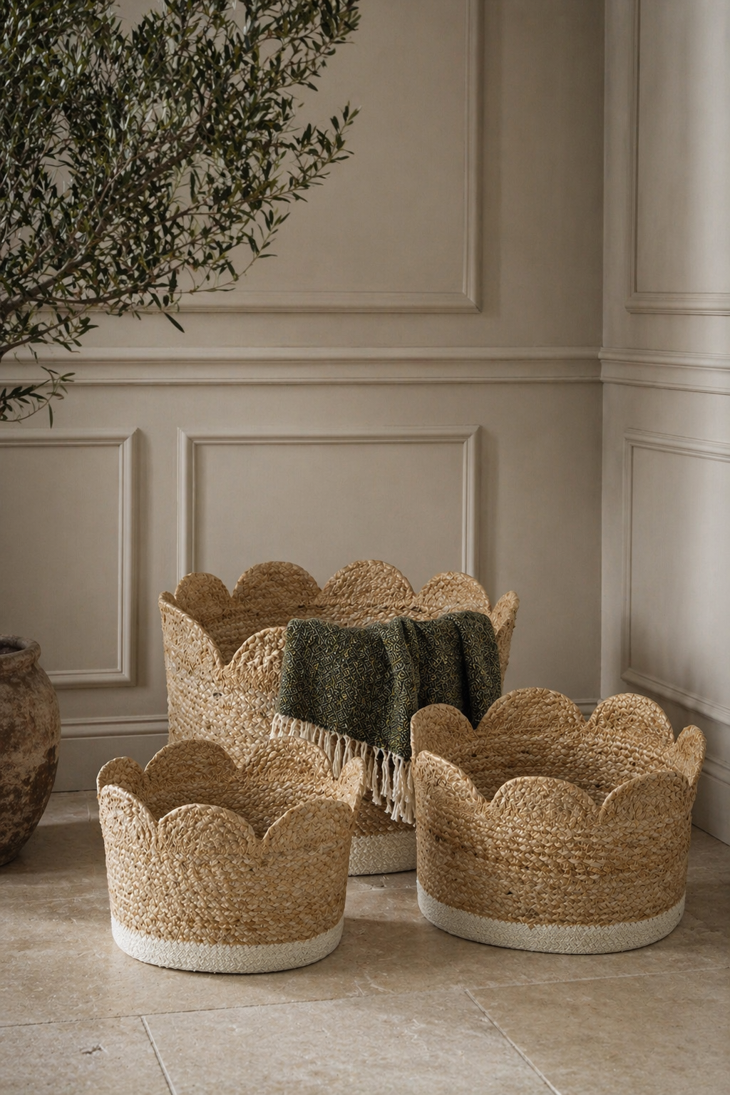Three woven seagrass storage baskets with scalloped edge on a stone floor with a neutral wall background