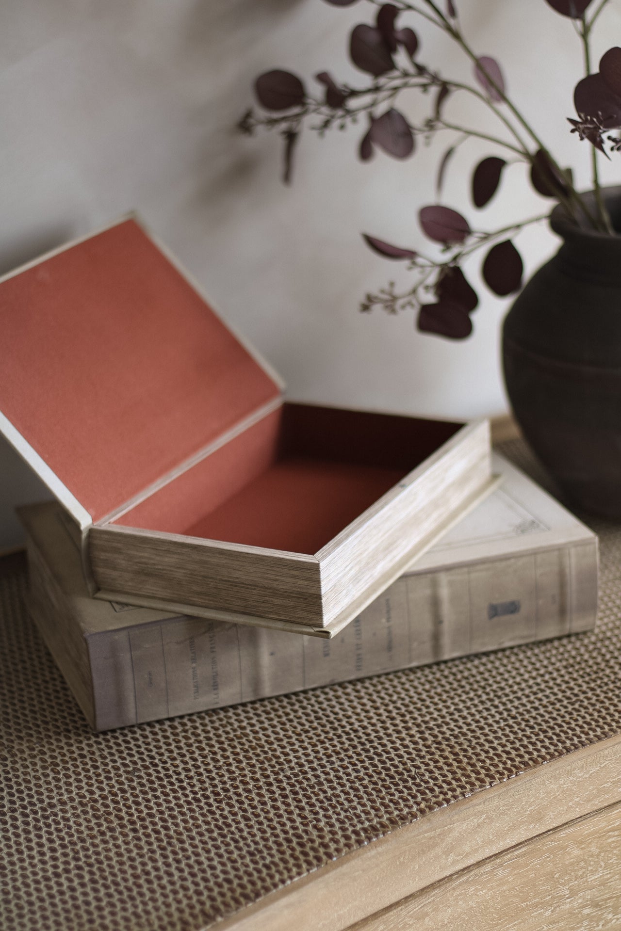 Wooden box with a red interior on a textured surface with a vase and branches in the background.