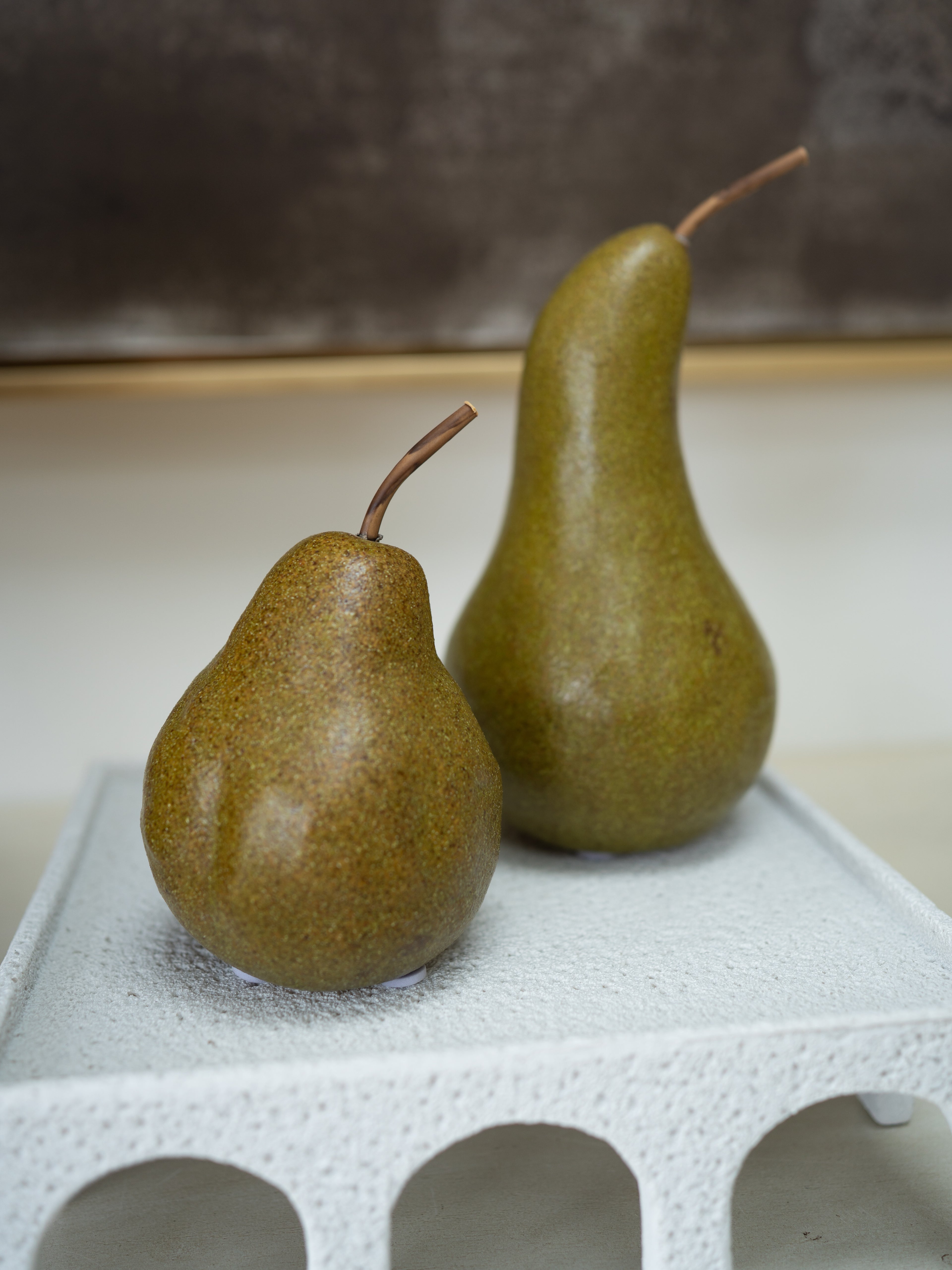 Two fresh pears, one smaller and one larger, with brown stems, displayed on a white textured ceramic tray against a neutral background.