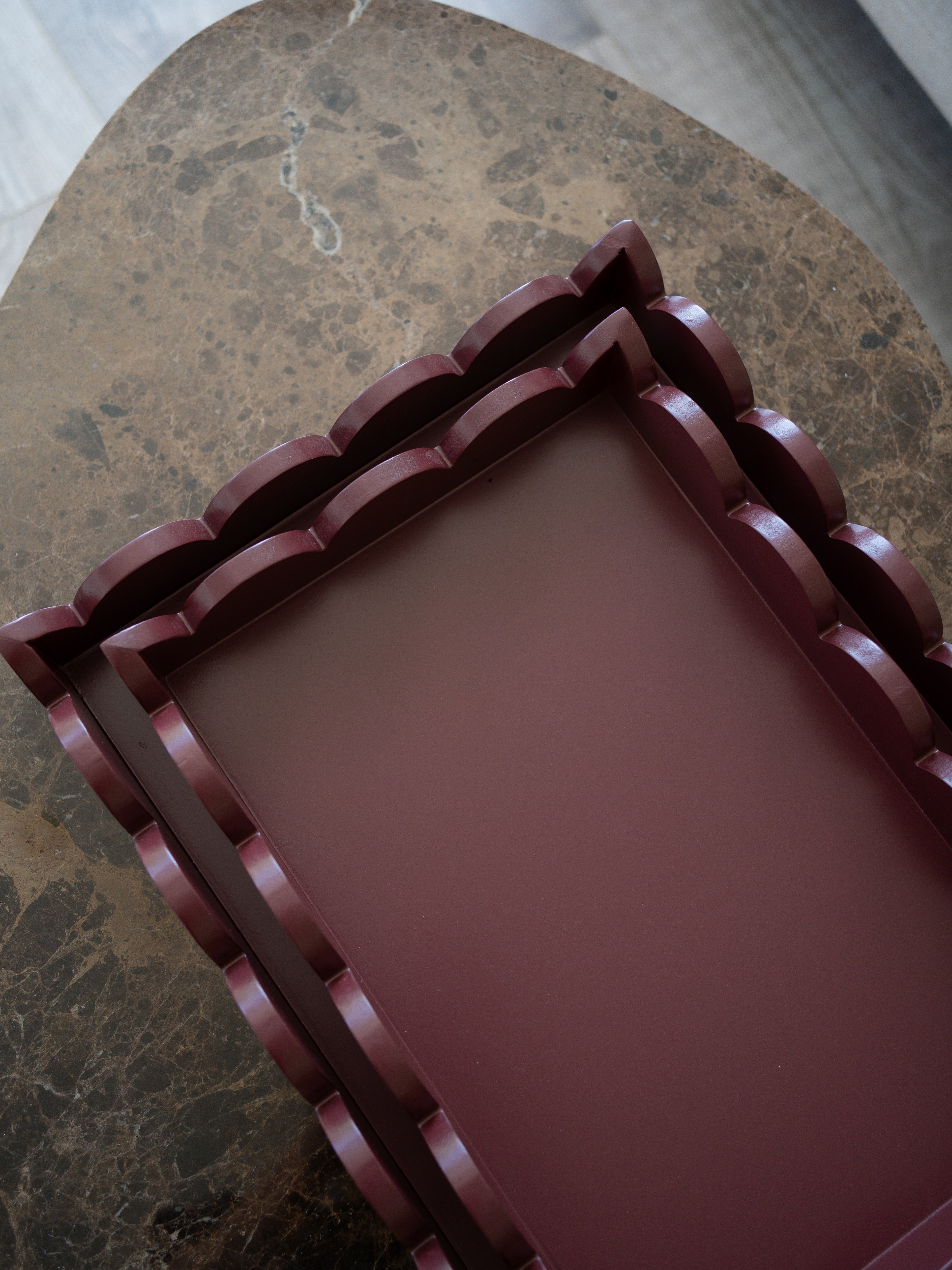 A rectangular tray with a scalloped, tiered border in a deep burgundy or plum-brown color, shown from an overhead angle on a brown marble surface.