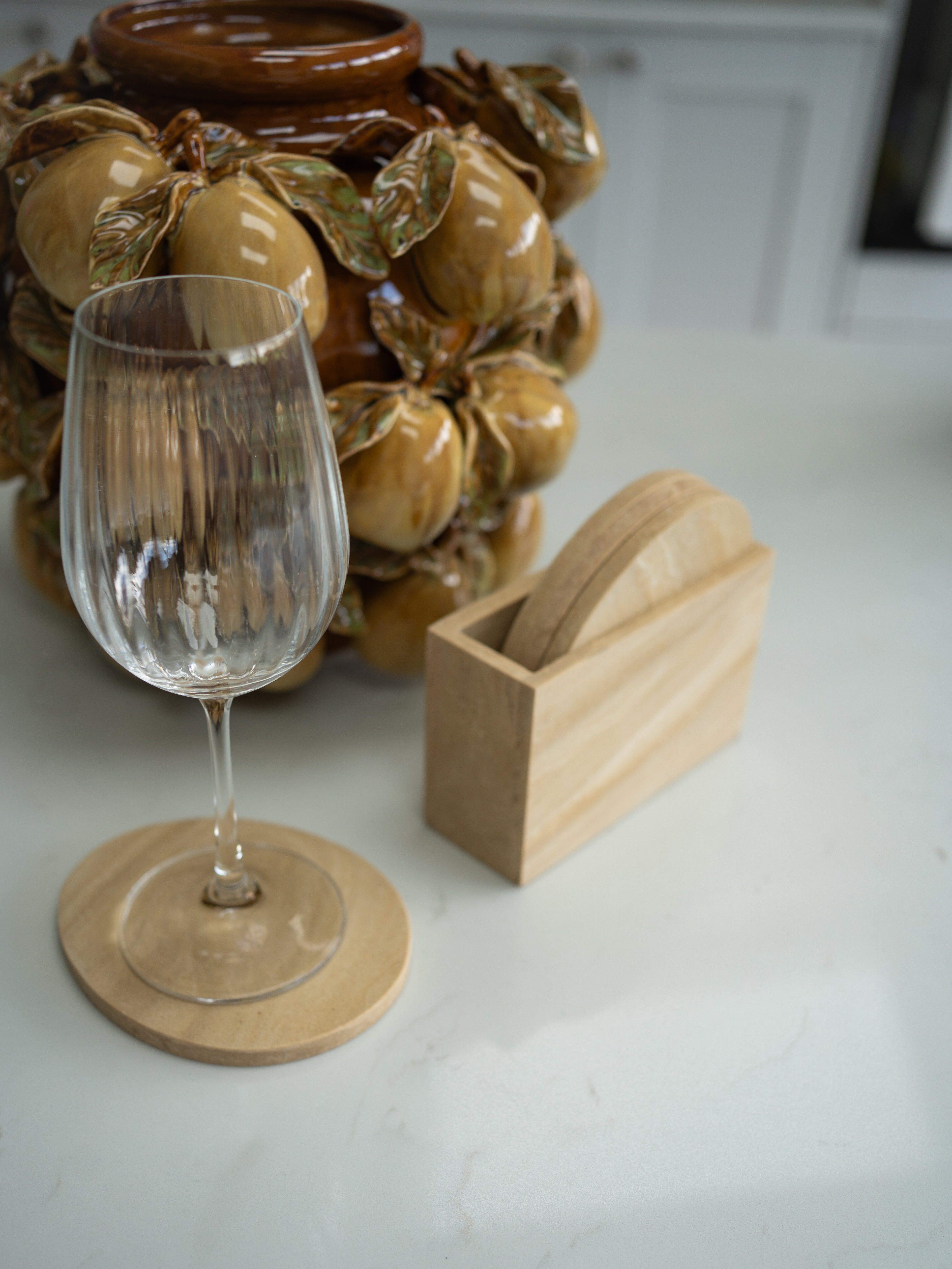 Wine glass on a travertine effect coaster with a decorative ceramic item in the background.