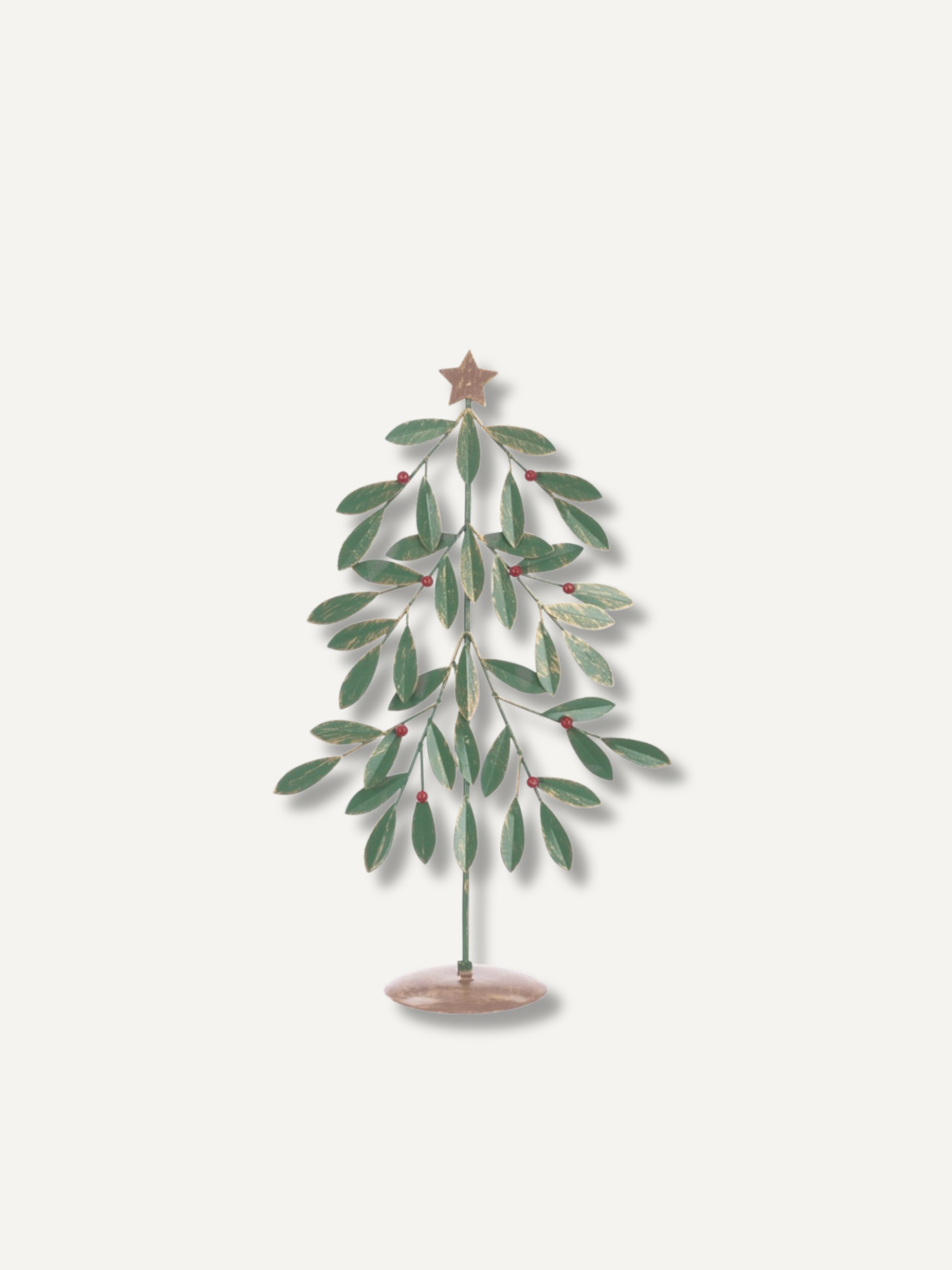 A decorative metal tree ornament with green leaves, small red berries, and a gold star on a light beige background.
