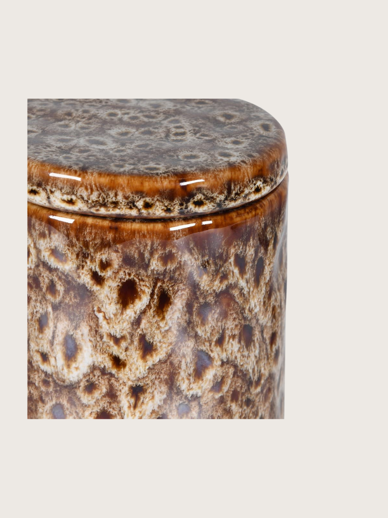 Decorative cylindrical container with a textured surface on a light gray background