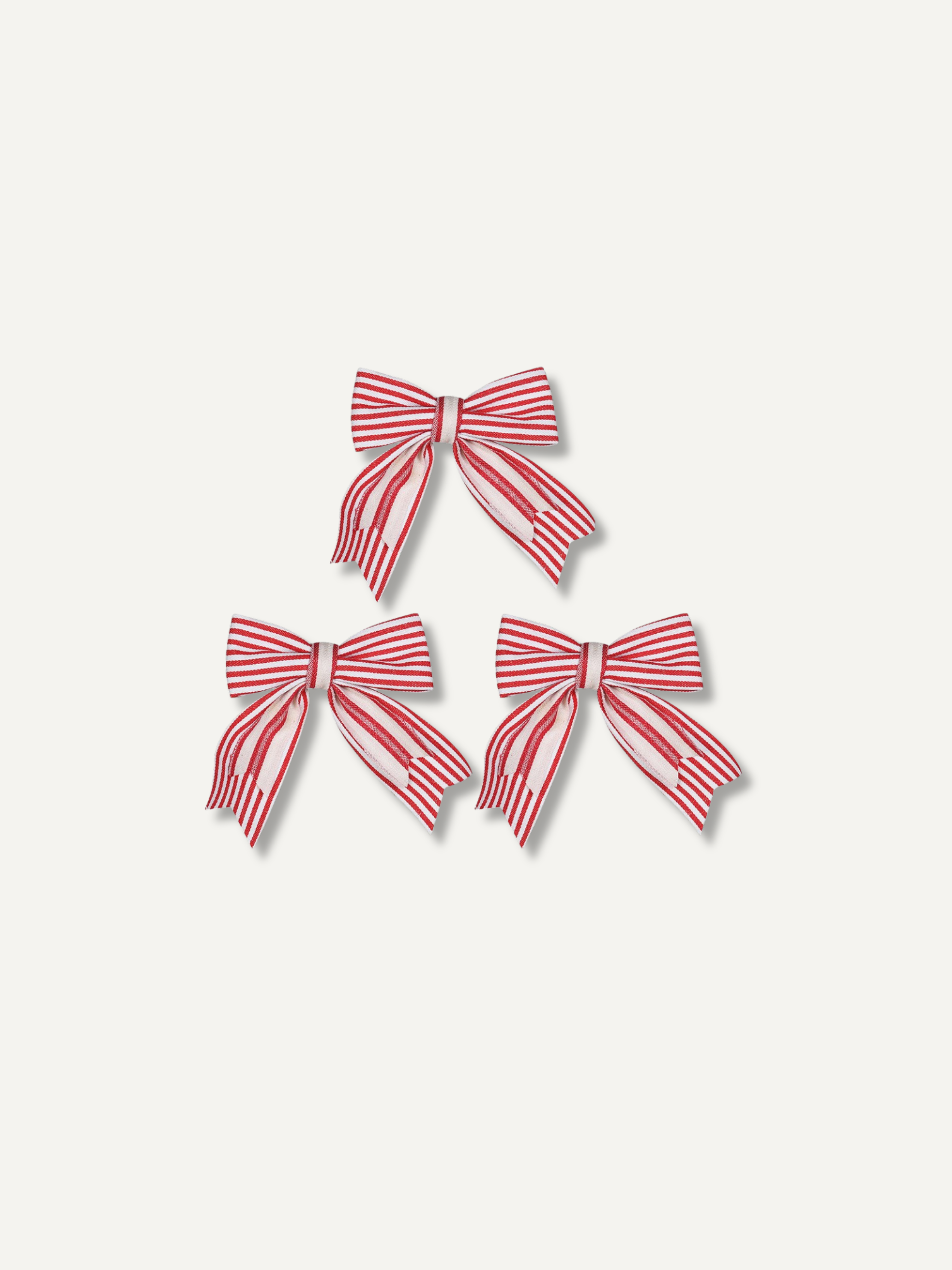 Three red and white striped fabric christmas bows arranged in a pyramid on a light beige background.