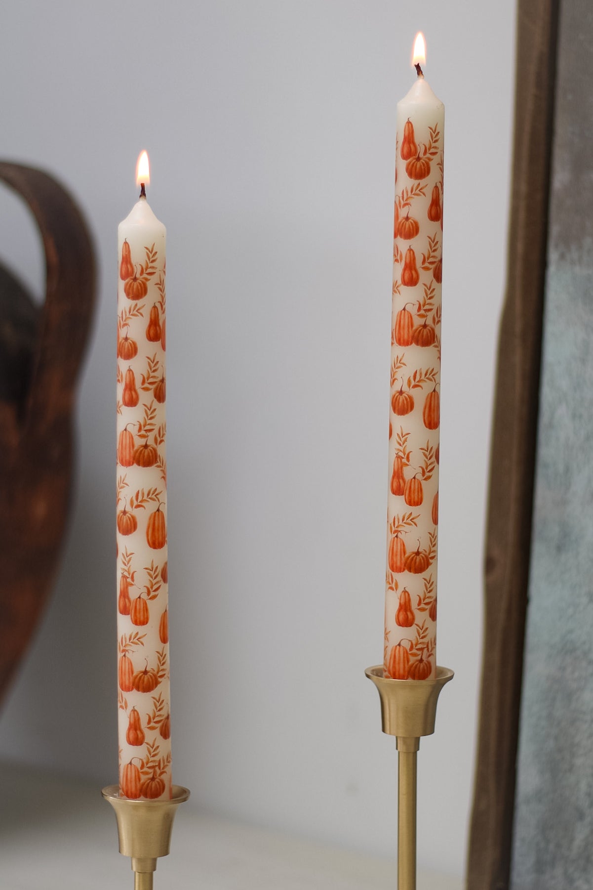 Two lit candles with pumpkin pattern in gold holders against a neutral background
