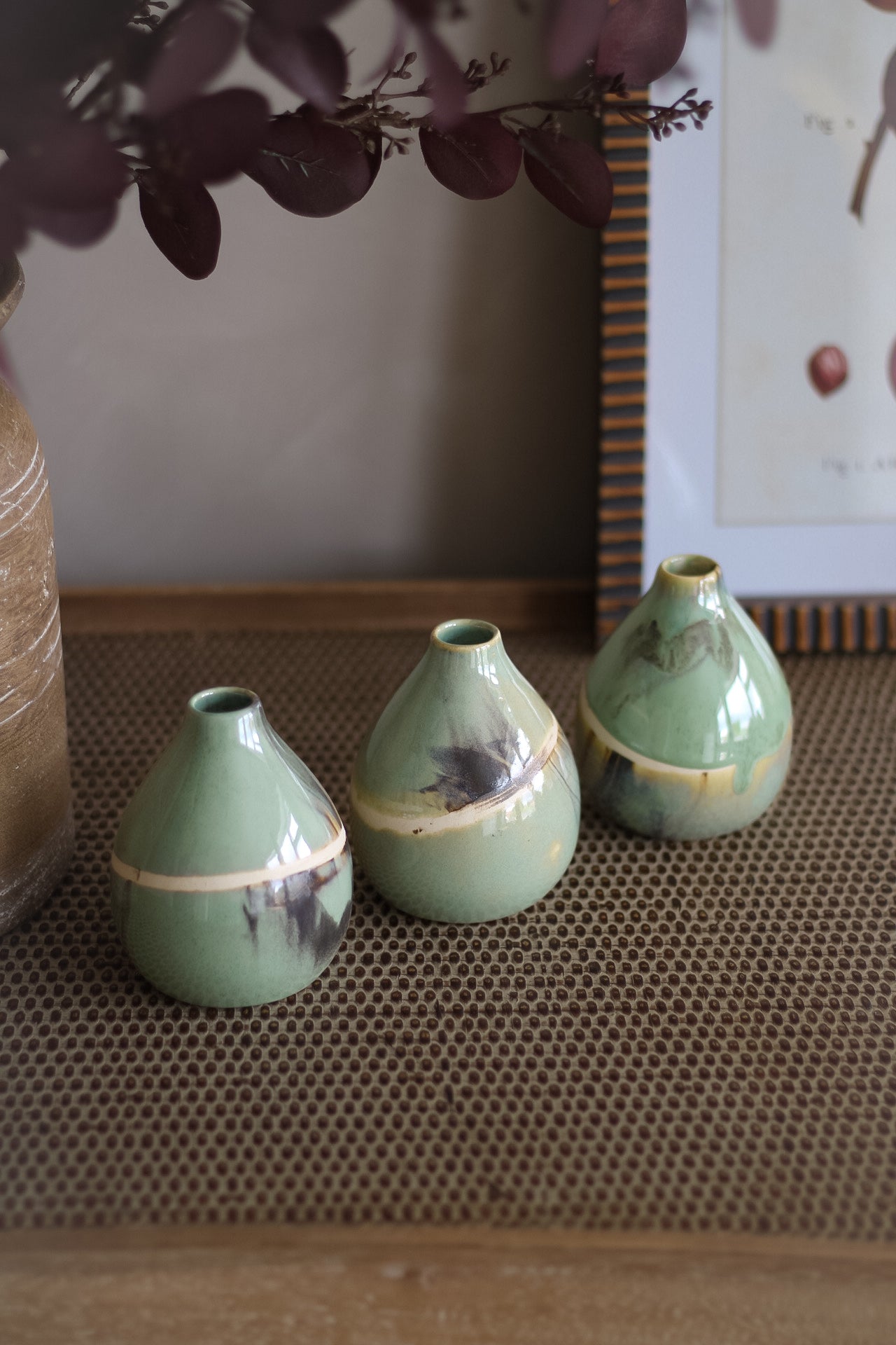 Three small sage green ceramic vases on a textured surface with a blurred background