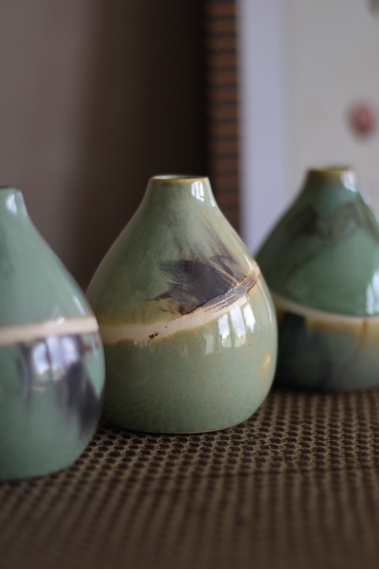 Three green ceramic bud vases on a textured surface with a blurred background