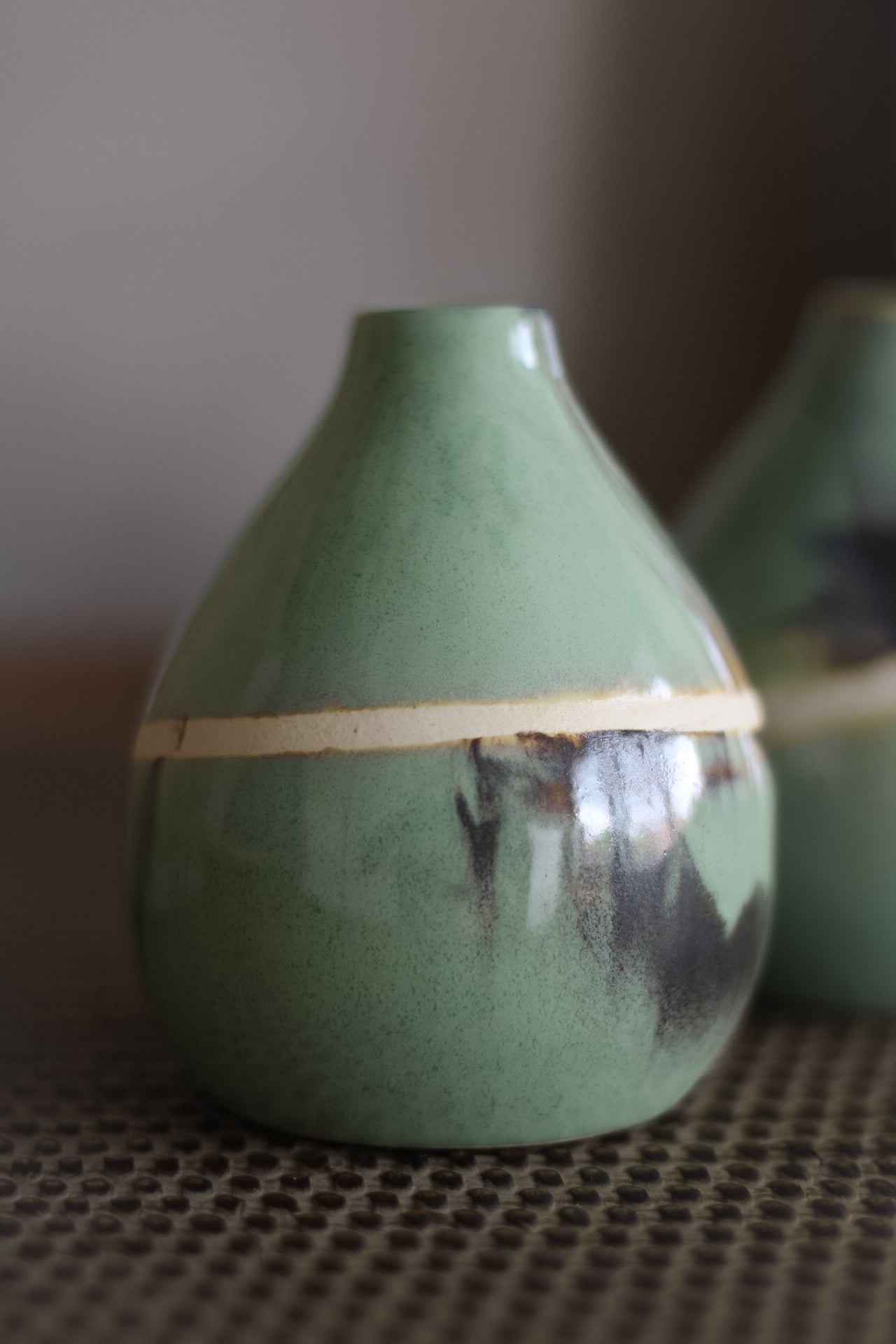 Green ceramic vase with a neutral band on a textured surface