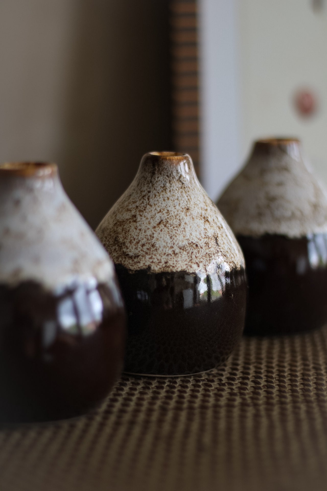 Three ceramic bud vases with speckled glaze on a textured surface