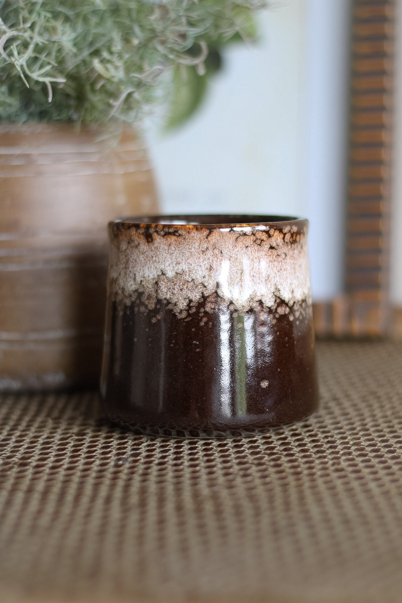 Ceramic candle holder with textured surface on a textured surface with a plant in the background